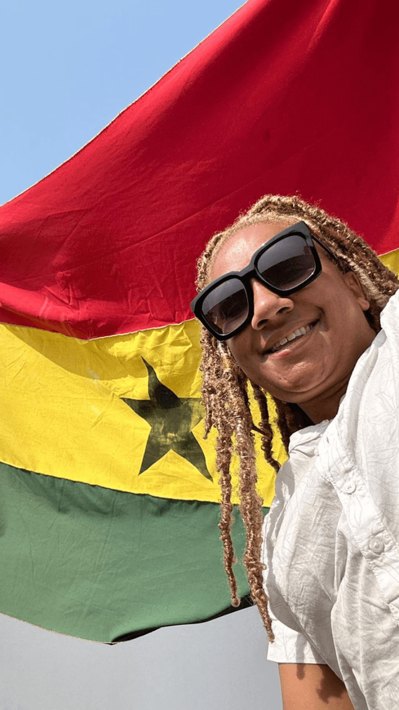 A woman smiling and wearing sunglasses, holding the Ghana Flag