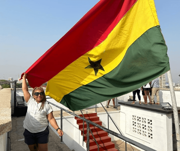 Woman holding The Ghana national flag with red, yellow, and green stripes and a black star in the center, at the rooftop of the Black Star Square