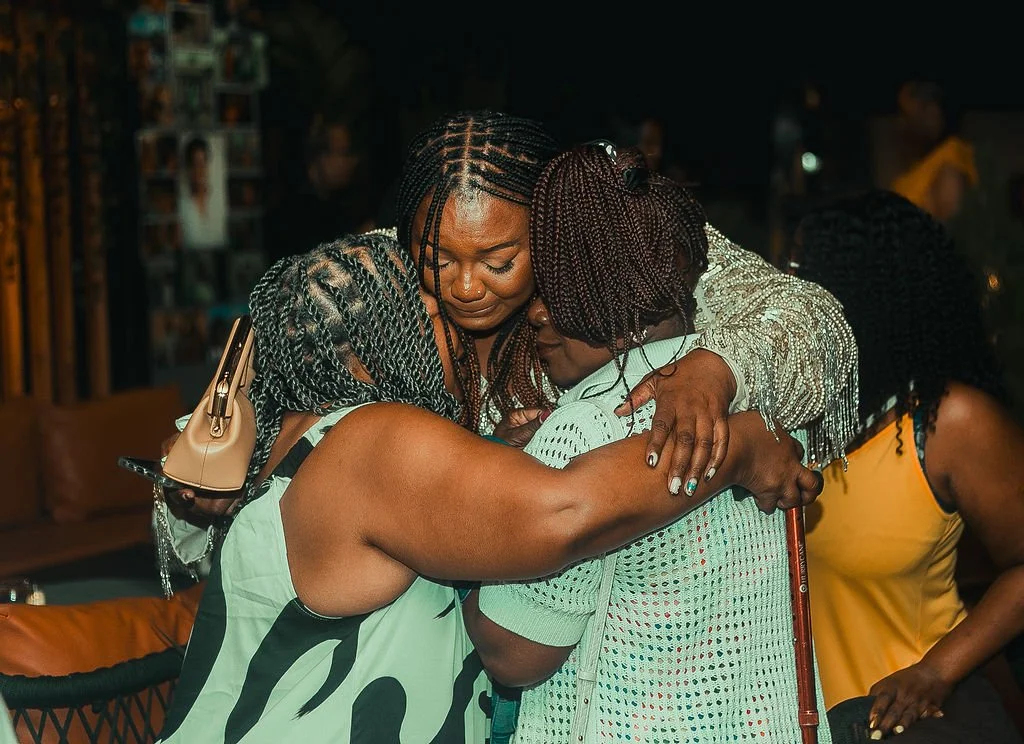 Three women share an emotional heartfelt hug at a private event during a heritage tour to Ghana.