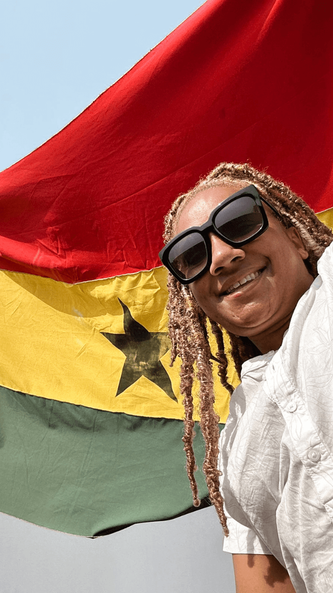 A woman smiling and wearing sunglasses, holding the Ghana Flag
