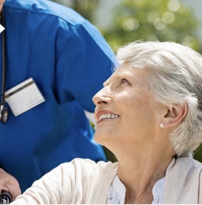 Elderly woman smiling at a healthcare worker in a blue uniform outdoors