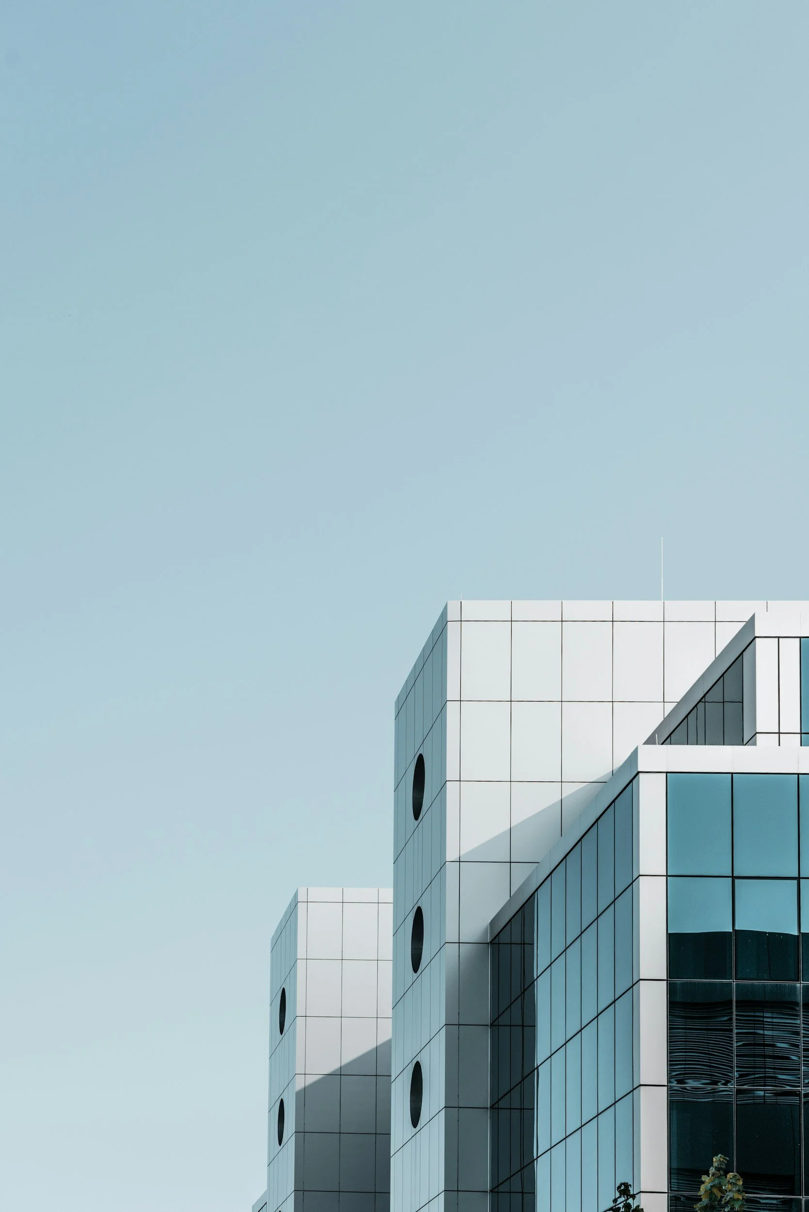 Modern white building with large glass windows and circular features against a clear blue sky.