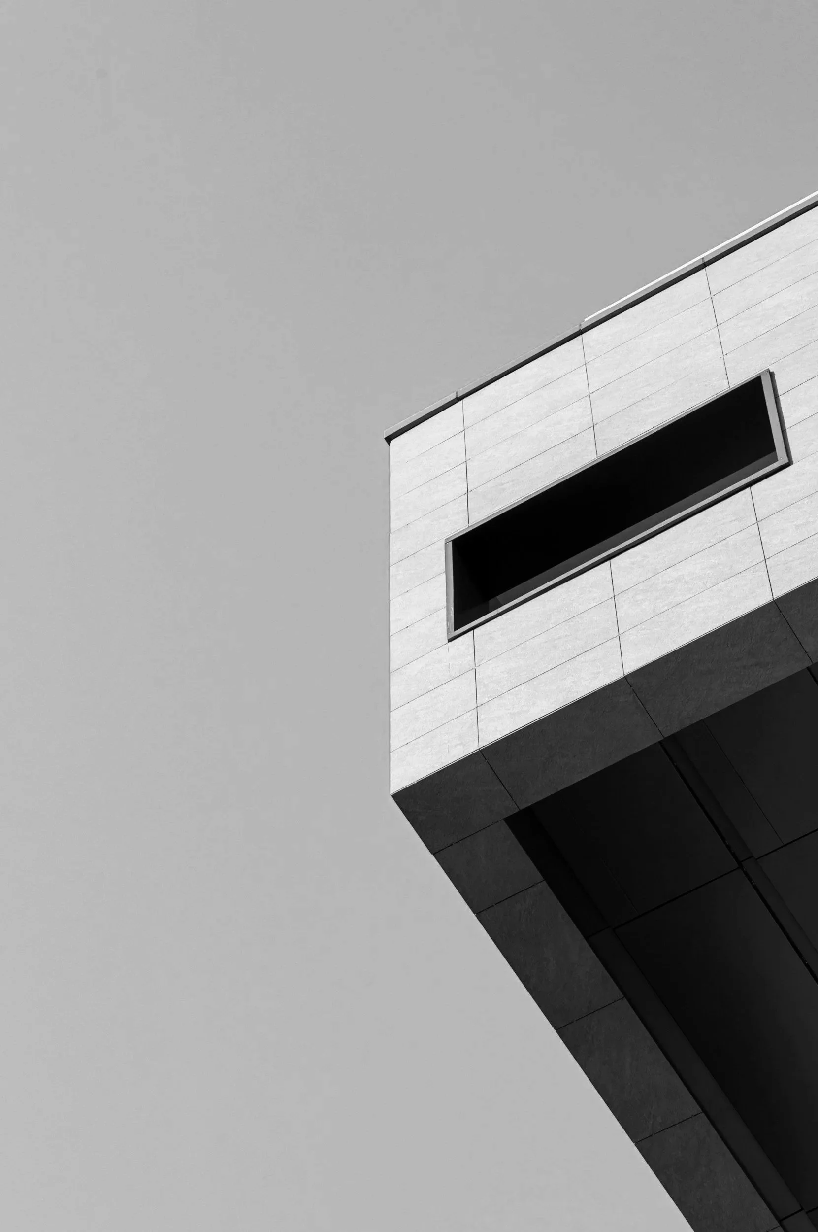 A modern building with a protruding section and rectangular windows, against a gray sky.