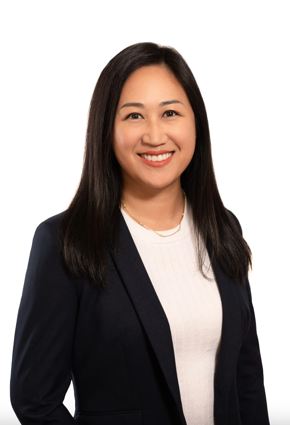 Professional portrait of a woman with long black hair, smiling, wearing a black blazer over a white top, against a white background.