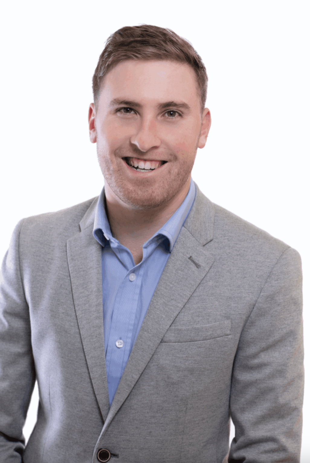 Headshot of a smiling young man in a light gray blazer and blue shirt against a white background.