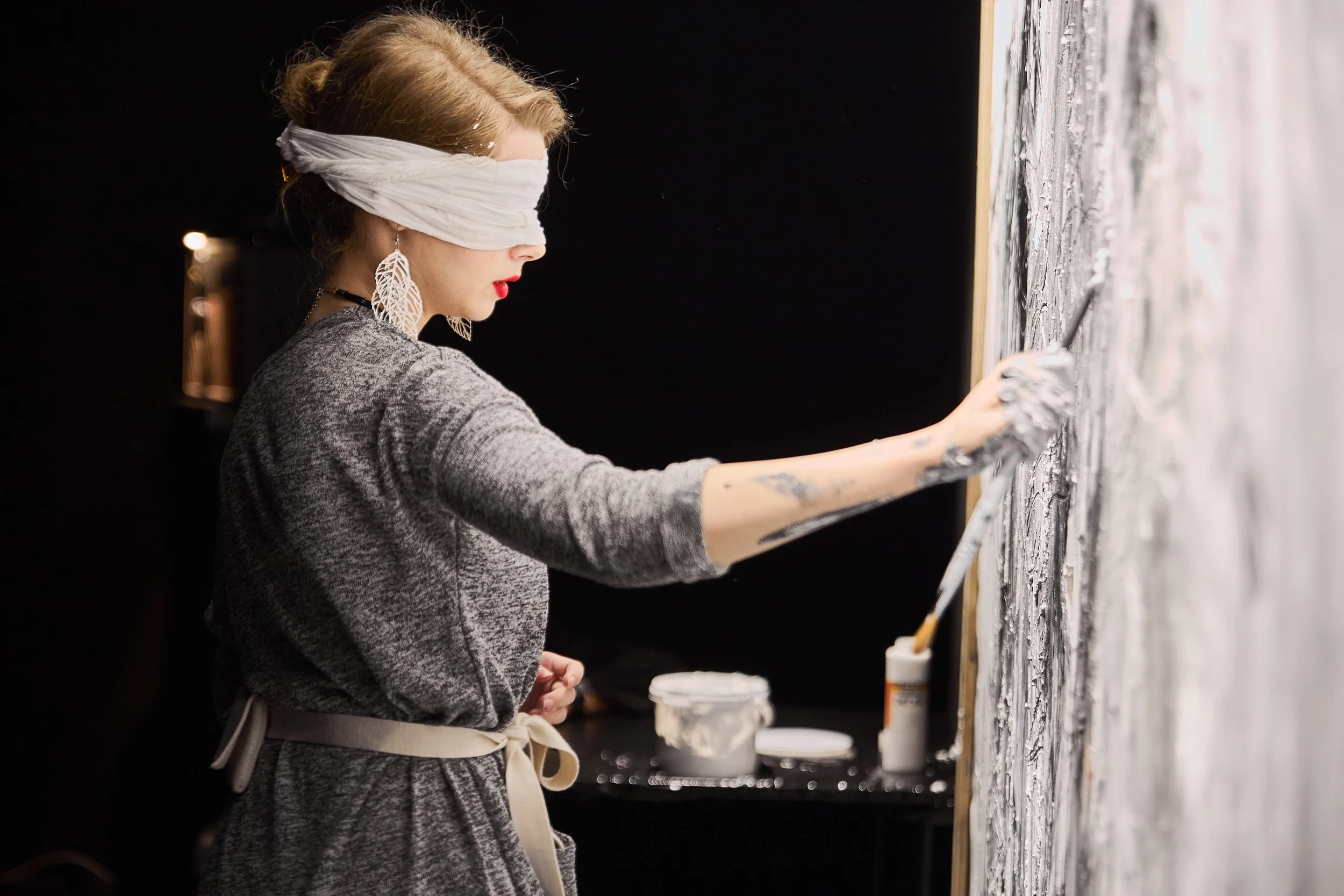 The she-artist blindfolded, painting on a canvas wall at an art event.