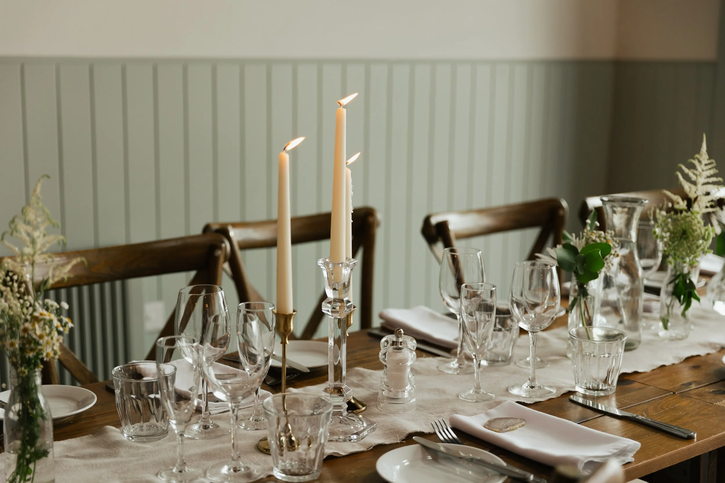 A dining table set for a formal meal with glassware, candles, and floral arrangements.