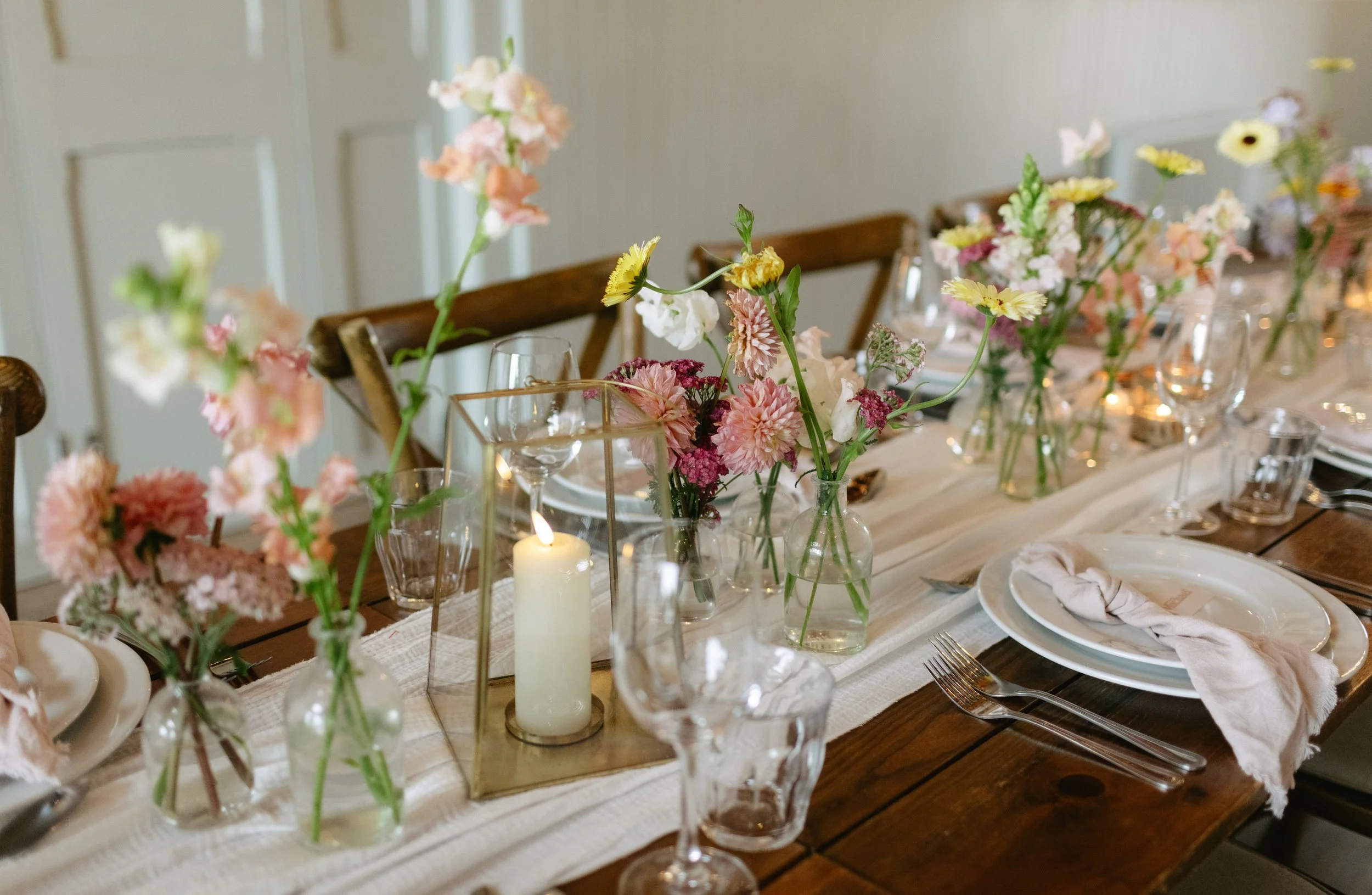 A dining table decorated with a floral centerpiece, candles, and elegant tableware in a well-lit room.