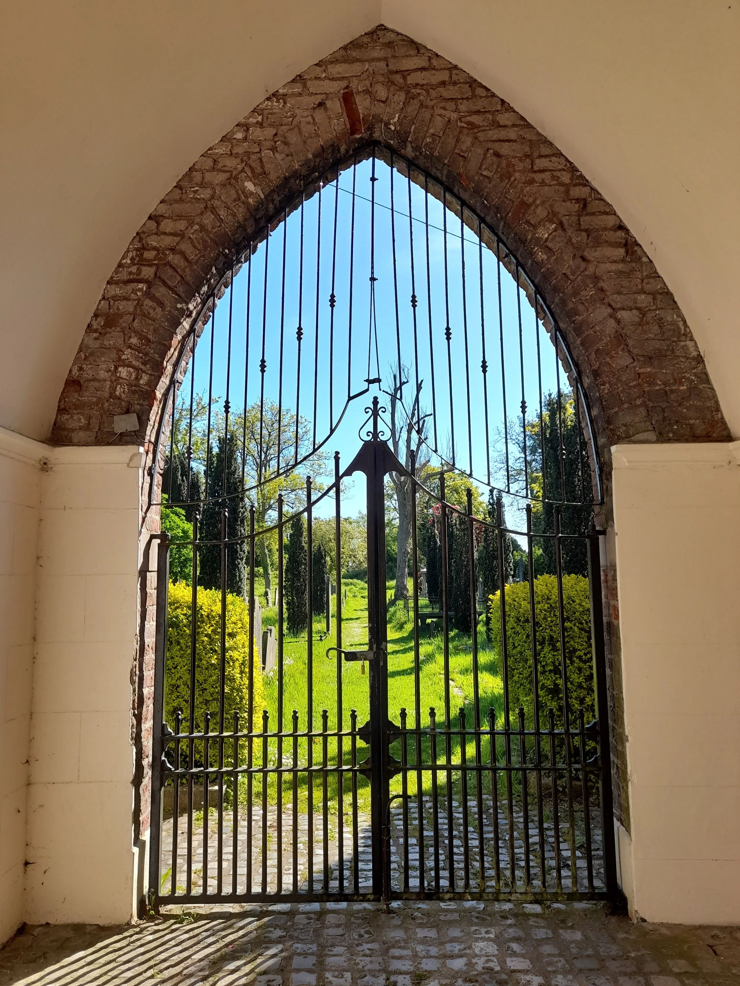 A portrait photograph of the inner gate to Friar's Bush Graveyard. The photograph depicts heavy, black wrought-iron gates set in an arched brick opening.