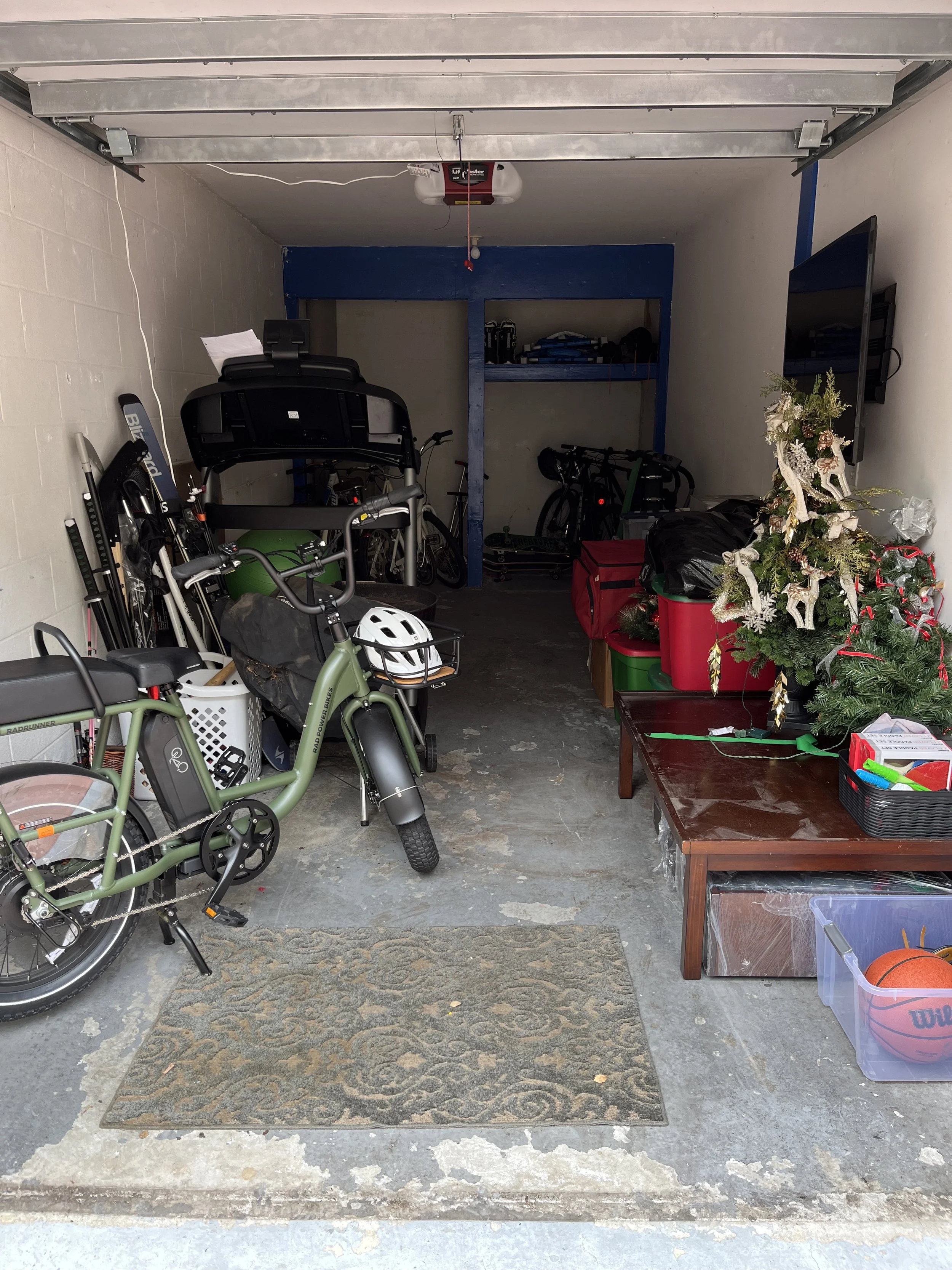 Garage with exercise equipment, a Christmas tree, storage boxes, and a coat rack.
