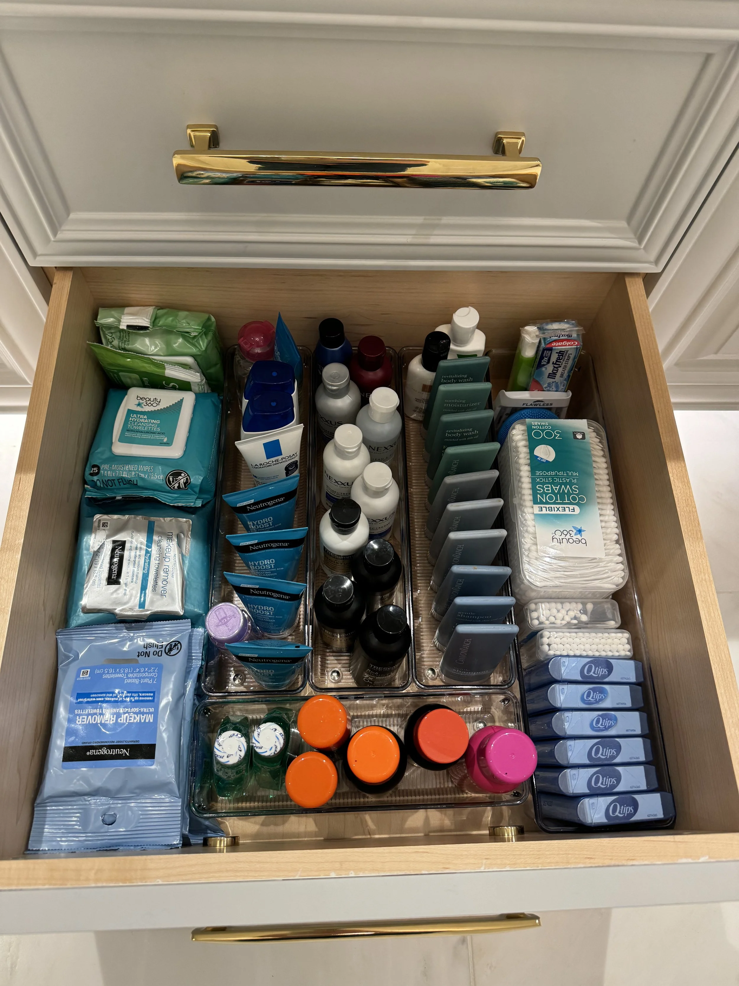 Organized drawer with various personal hygiene and skincare products including bottles, wipes, cotton swabs, and cosmetic items.