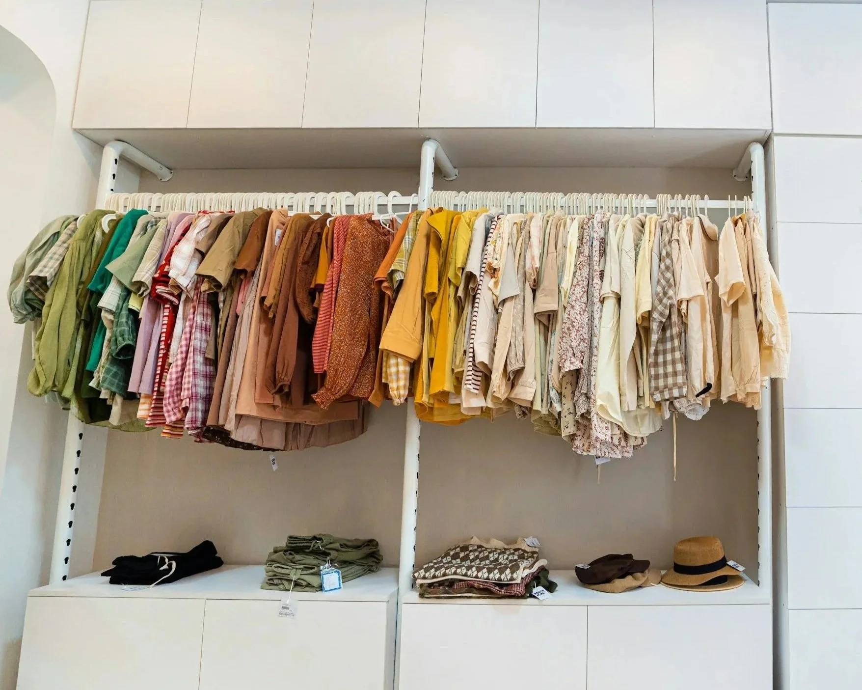Clothing rack with various shirts hanging, and folded pants and hats on shelves below.