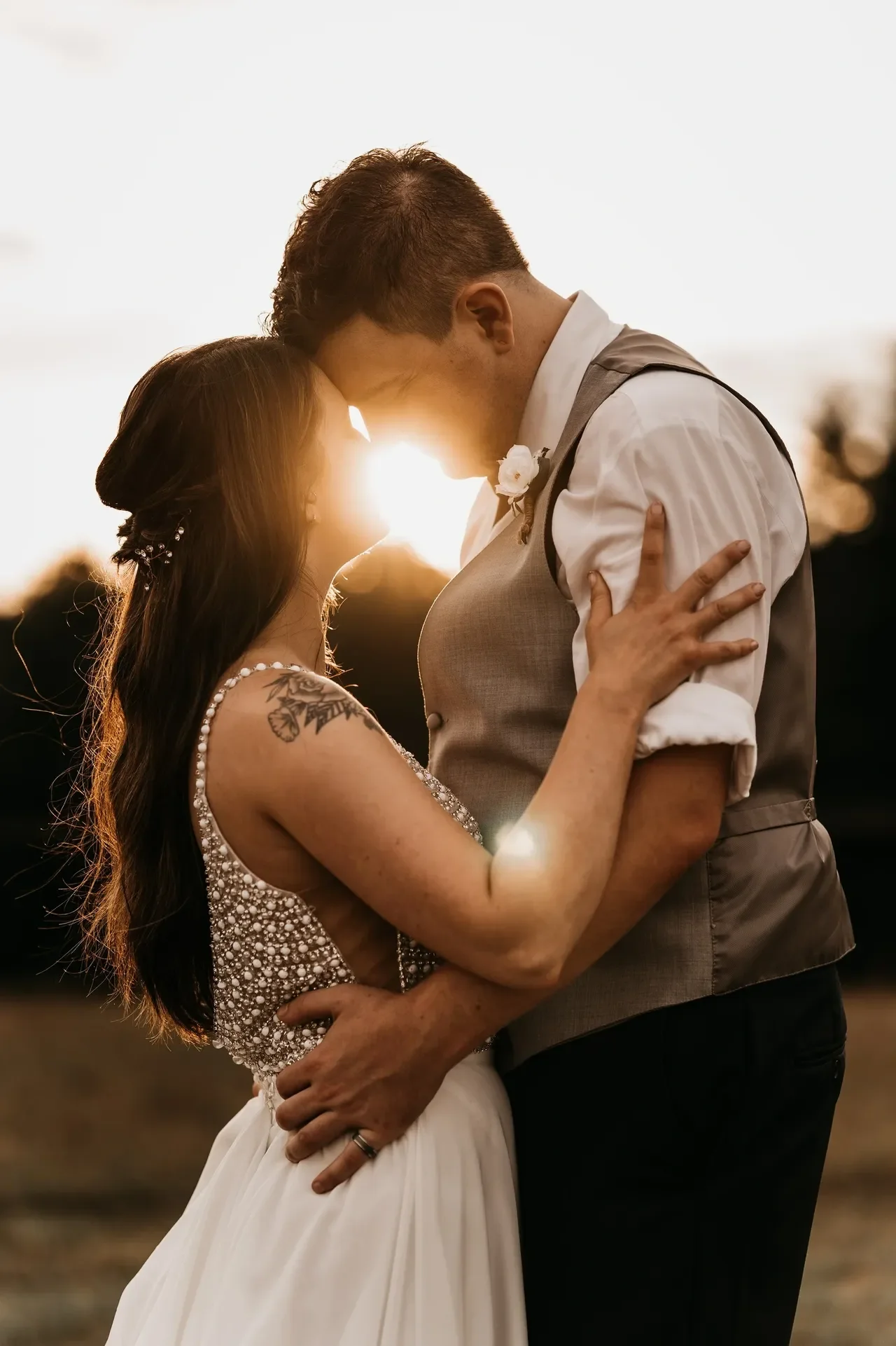 Newlyweds embrasing at sunset with the sun between them.