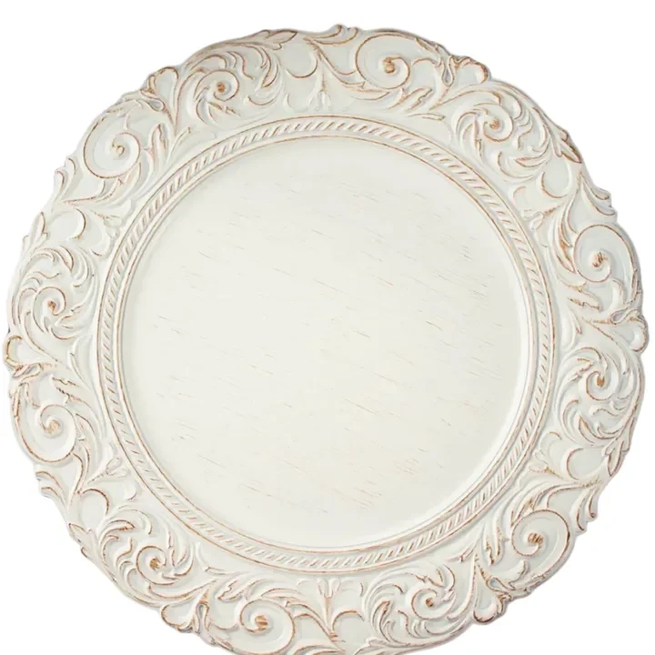 A decorative round white plate with ornate, scrollwork edges in a distressed white and gold finish.