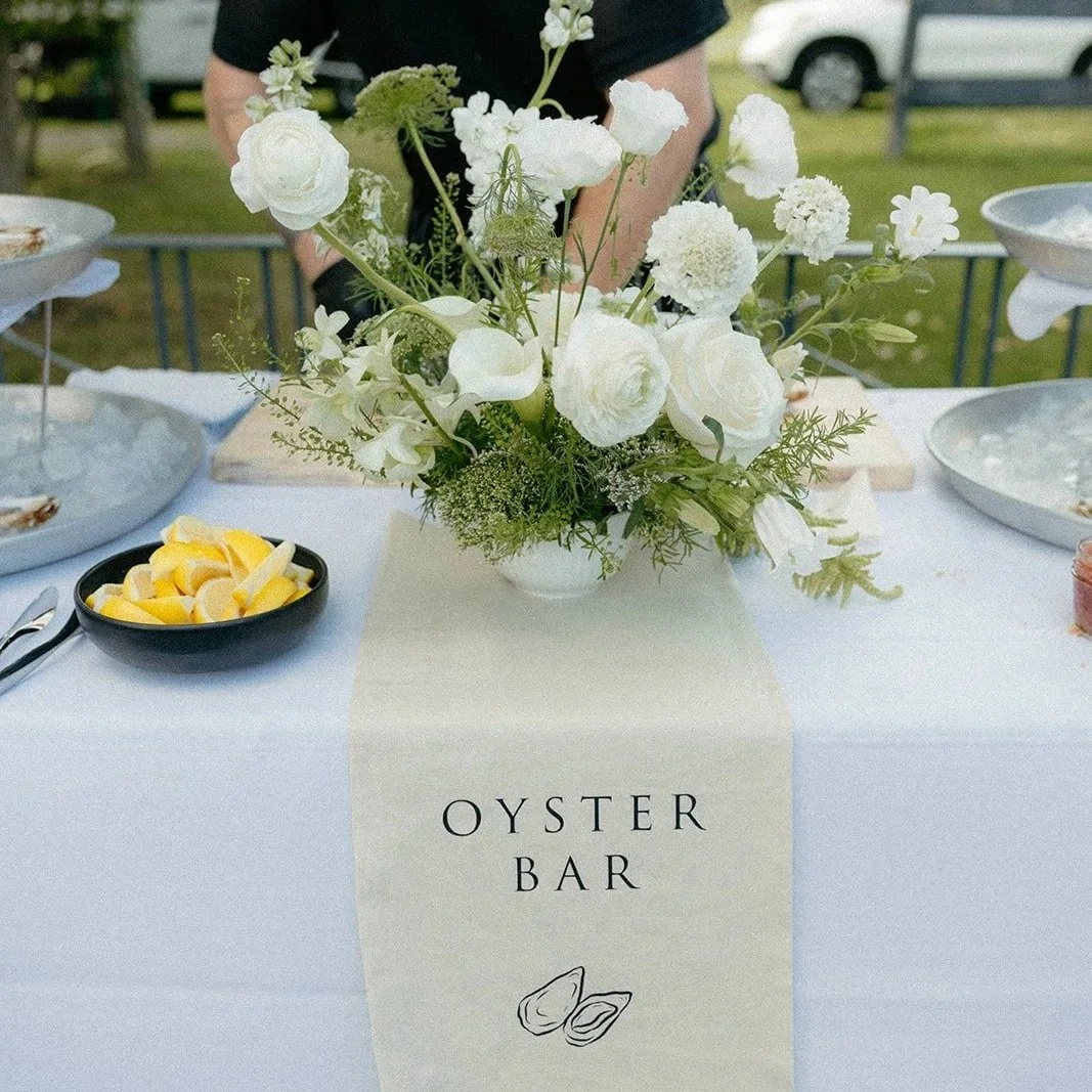 Oyster Bar sign draped over a table with lemons in a dish and a white and green floral arrangement.