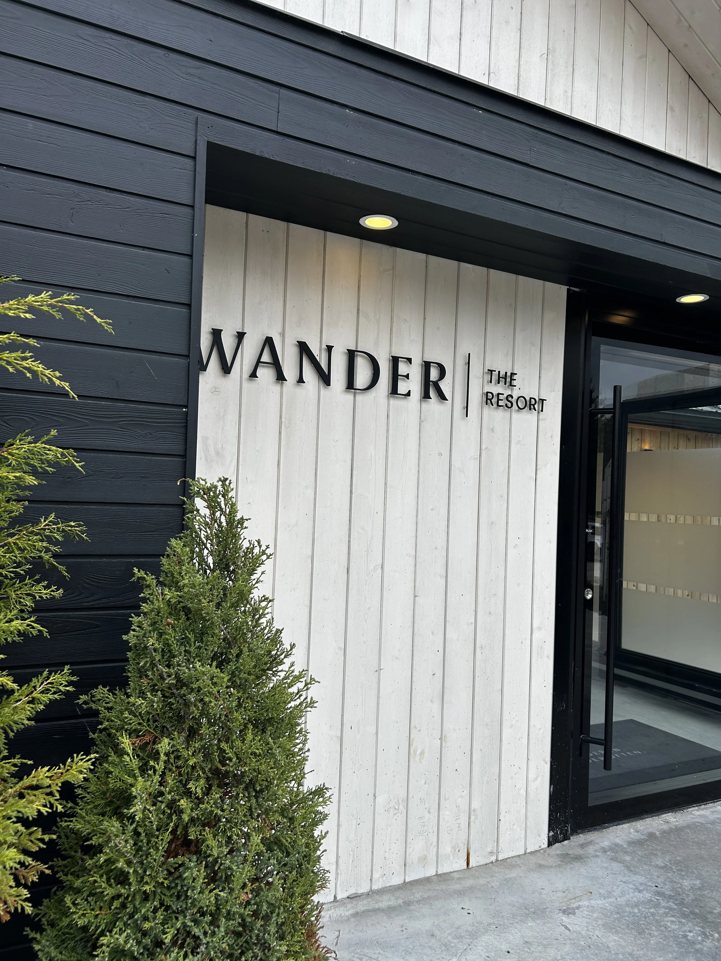 Main entrance to Wander the Resort. White washed and black stained modern look with evergreens to the side.