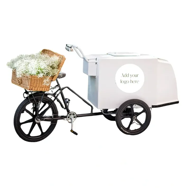 A black bicycle with a wicker basket filled with white flowers attached to the handlebars, connected to a white cargo cart with a placeholder for a logo.