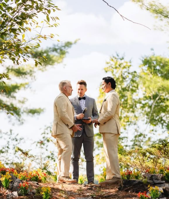 Wedding officiant and two grooms in beige in a wooded area