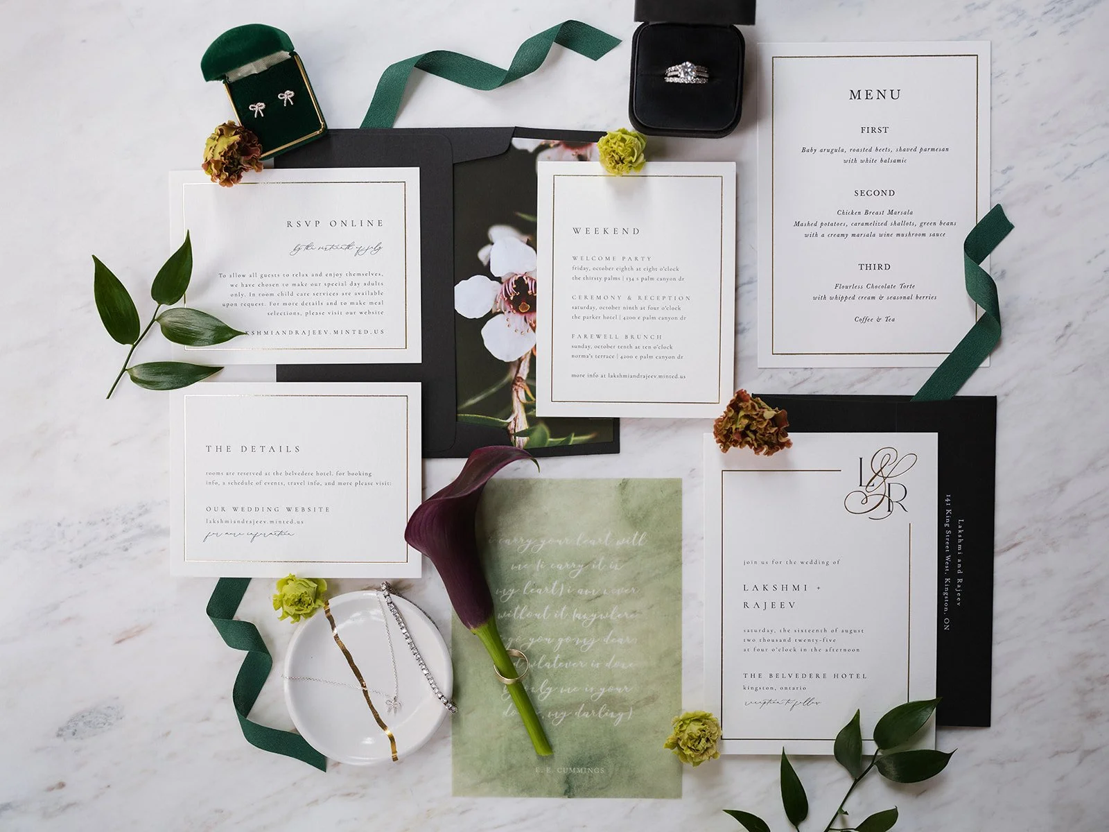 Wedding invitation suite with floral accents, featuring RSVP, weekend events, menu, and details cards, surrounded by flowers, jewelry, and greenery on a white marble surface.