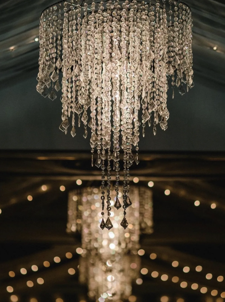 Chandelier with multiple tiers of hanging crystals decorated with small lights in the background.
