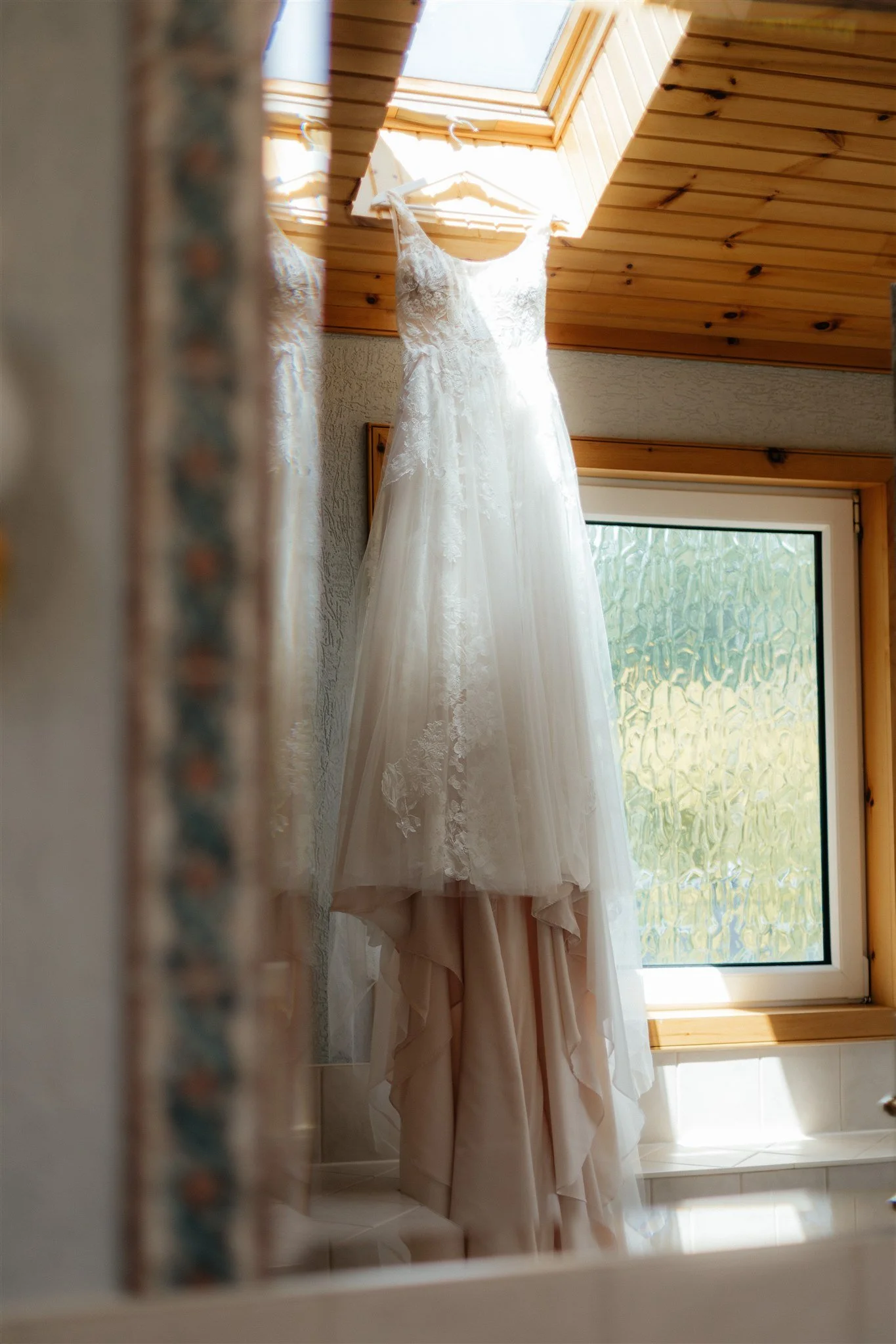 Wedding dress hanging near a window in a wooden ceiling room.