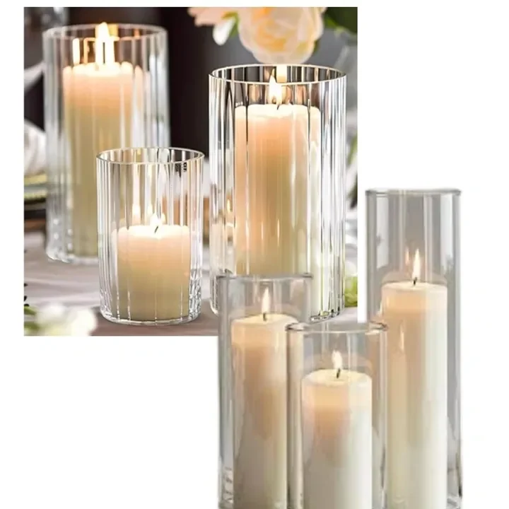Several tall clear glass candle hurricanes of various heights with lit white candles inside, arranged on a table for decor.