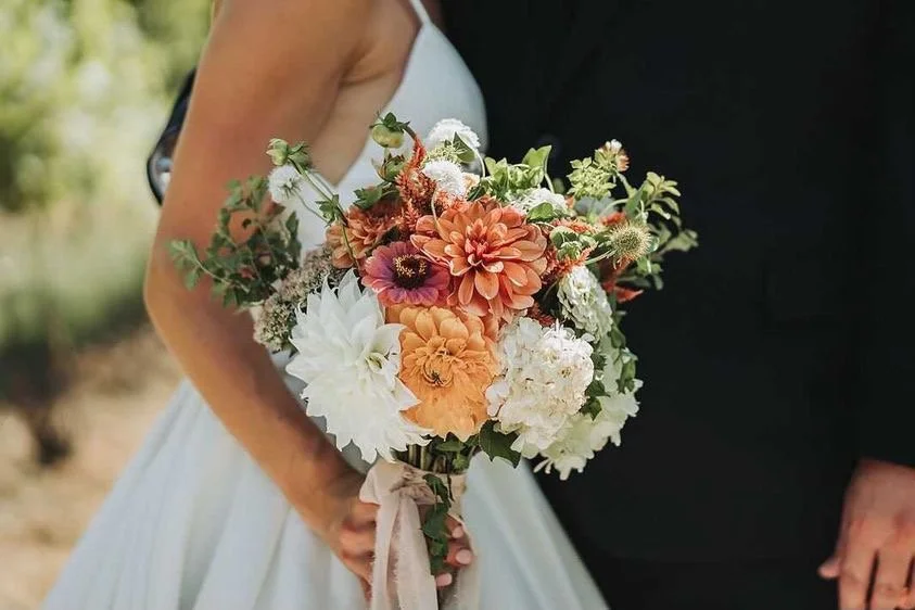 Bride and groom holding a bouquet of orange, white, and pink flowers on their wedding day.
