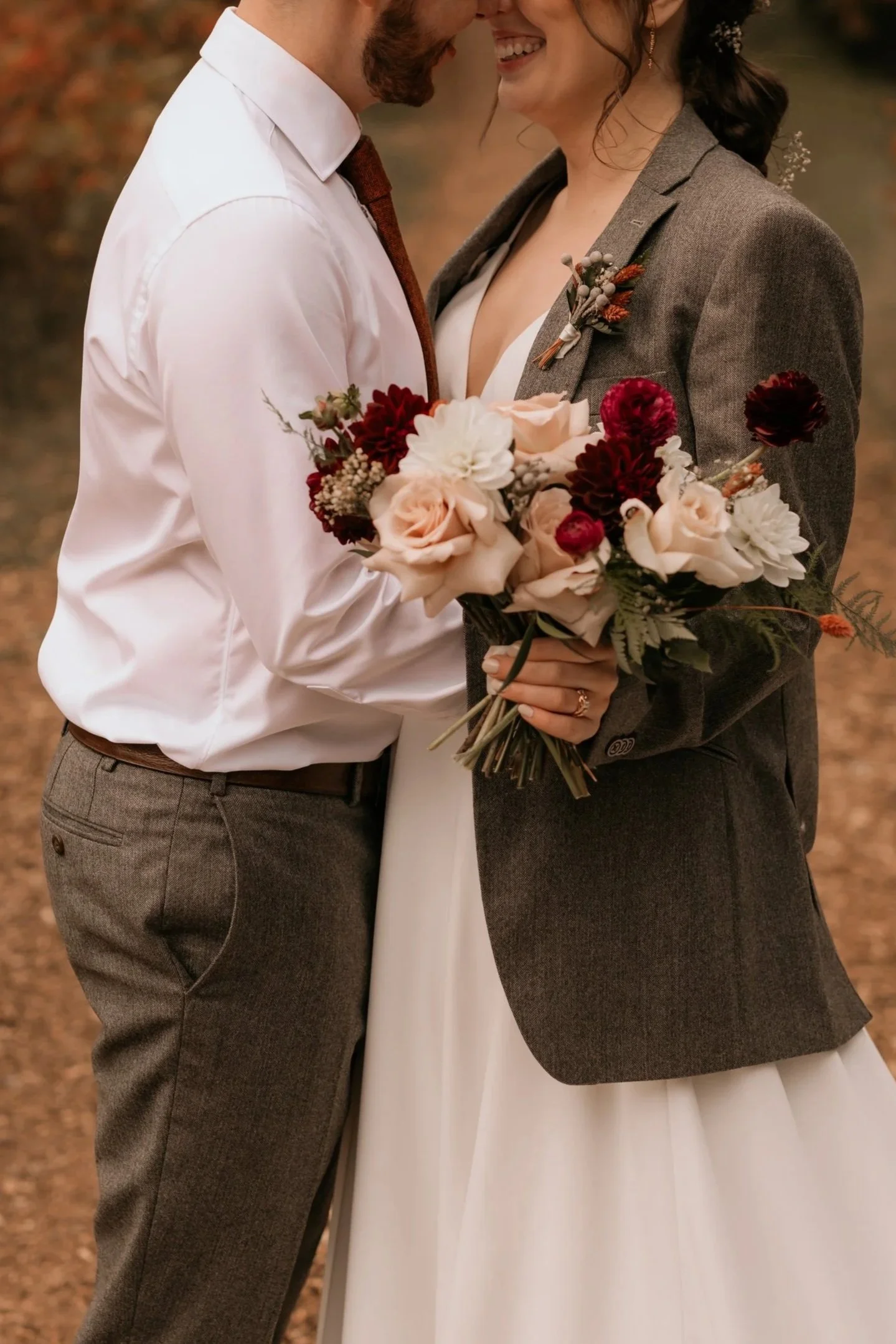 Groom in white shirt, bride wearing rooms tweed jacket and holding a colourful pink and burgundy bouquet.