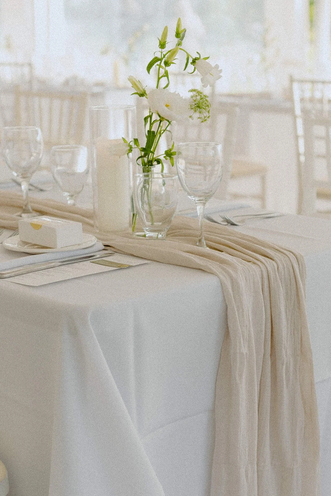 A harvest table draped in whites and creams with, florals-glassware and pillar candles.