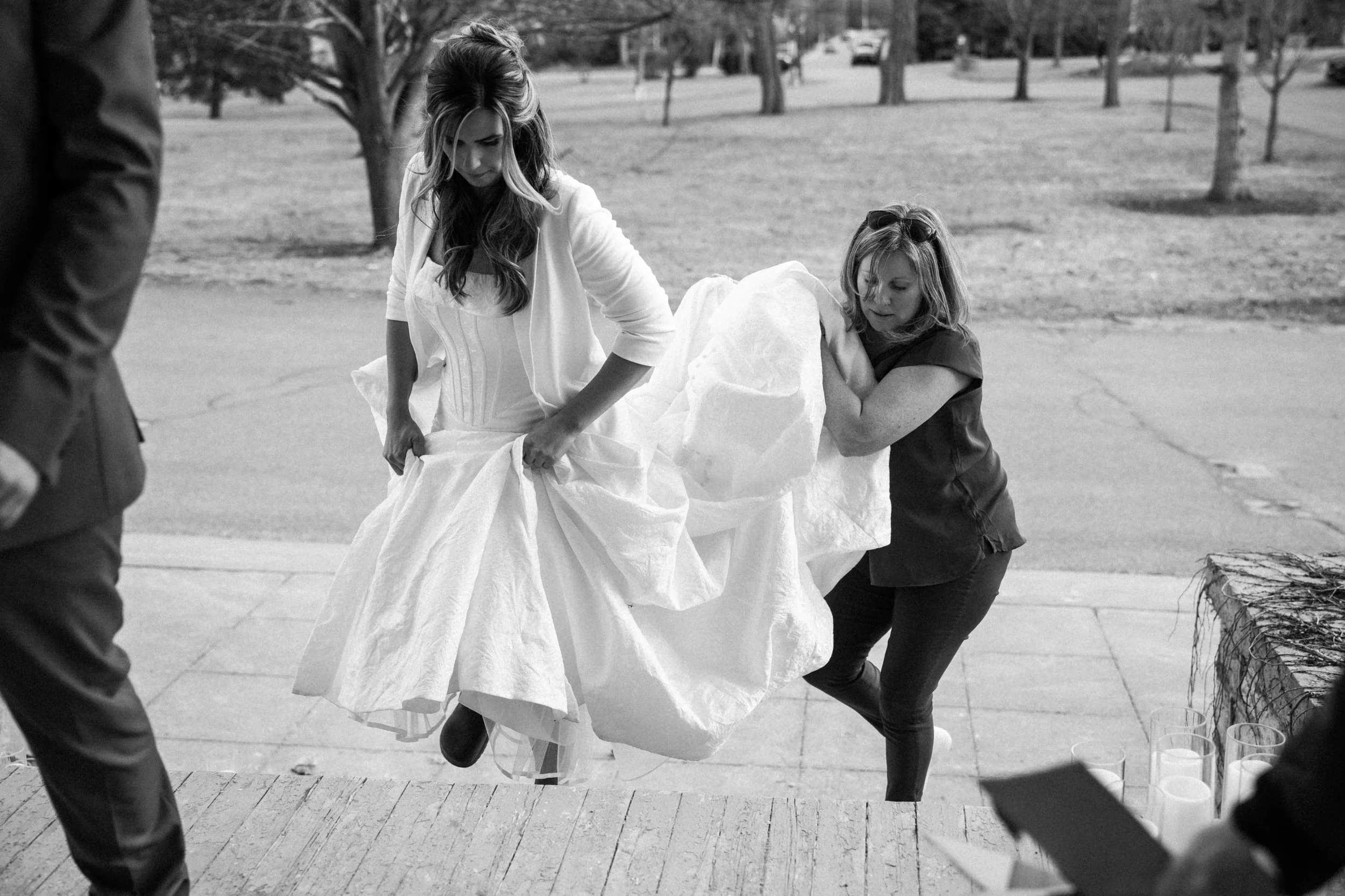 Kingston Wedding Planner helping a bride in a white wedding dress with a long train coming up outdoor stairs.