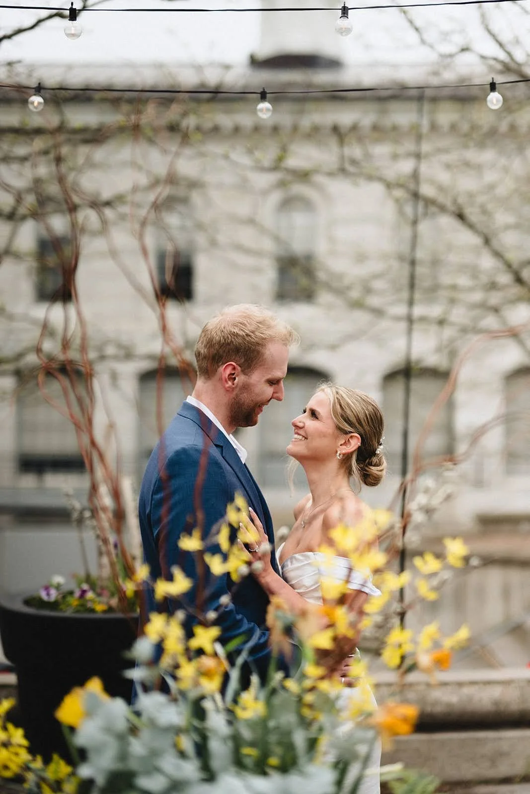 Newlyweds embrasing behing forsythia behind city hall