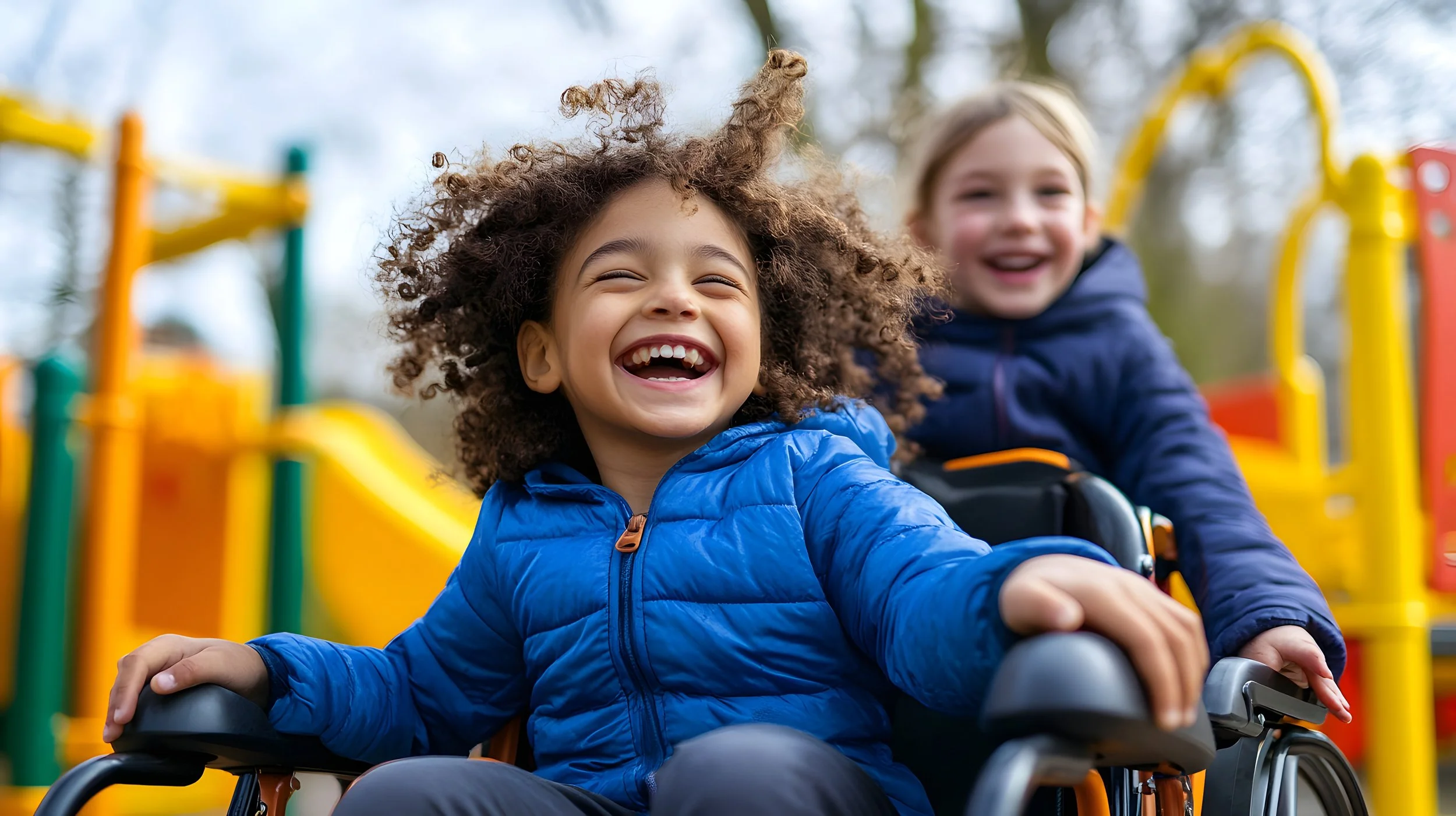 Two children, a girl with curly hair and a boy with straight hair, both smiling and enjoying themselves on playground equipment outdoors.