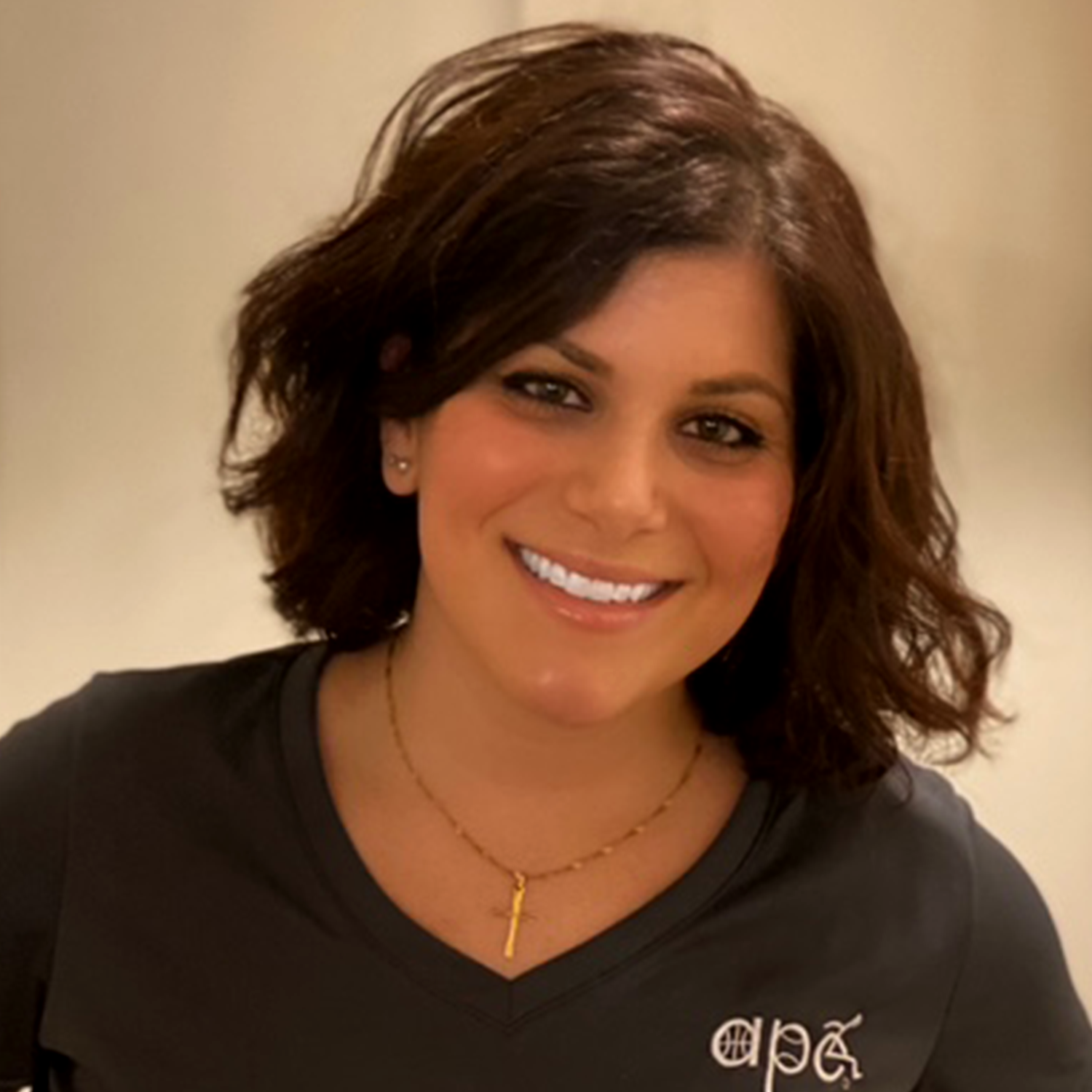A woman with shoulder-length brown hair smiling, wearing a black shirt and a gold necklace.