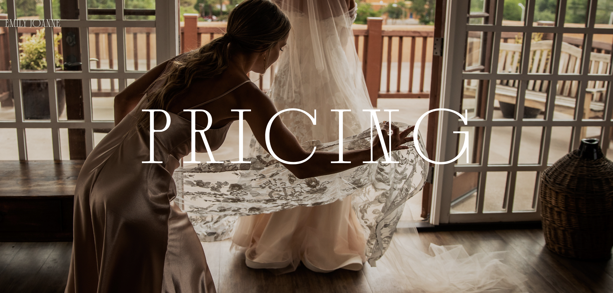 A woman in a satin dress helping another woman in a wedding gown adjust her dress at a doorway, with a backyard visible outside.