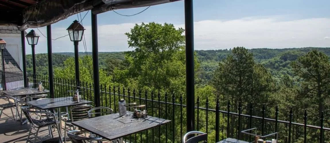 Outdoor patio seating at Skybar Gourmet Pizza in Eureka Springs, Arkansas, offering a panoramic view of the lush, rolling Ozark mountains and treetops from a high balcony.