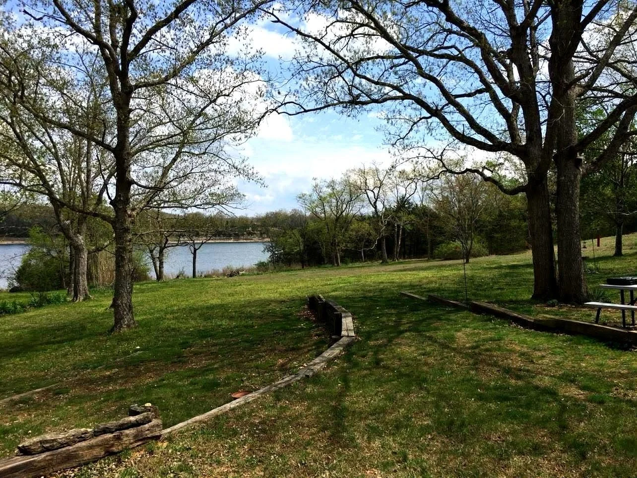The peacefulback yard of Martha's View  with trees, grass, and a view of the water where the back yard leads to under a partly cloudy sky.