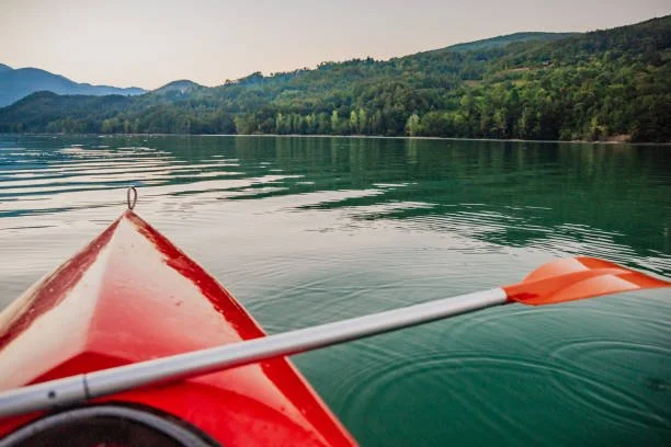 View from a red kayak on a calm lake with green hills and mountains in the background.