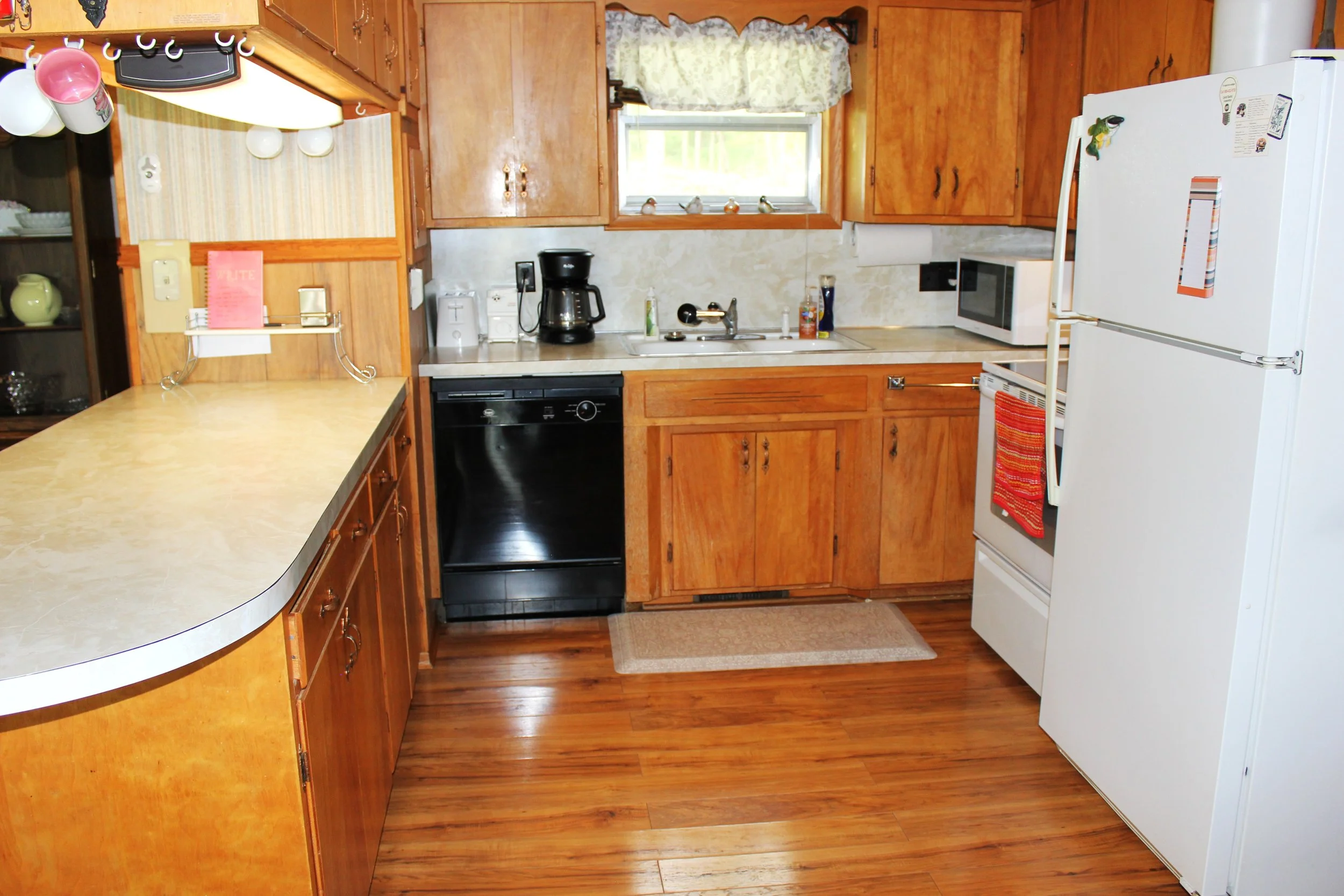 A kitchen with wooden cabinets, a white refrigerator, a microwave, a coffee maker, and a window above the sink showing some outdoors.