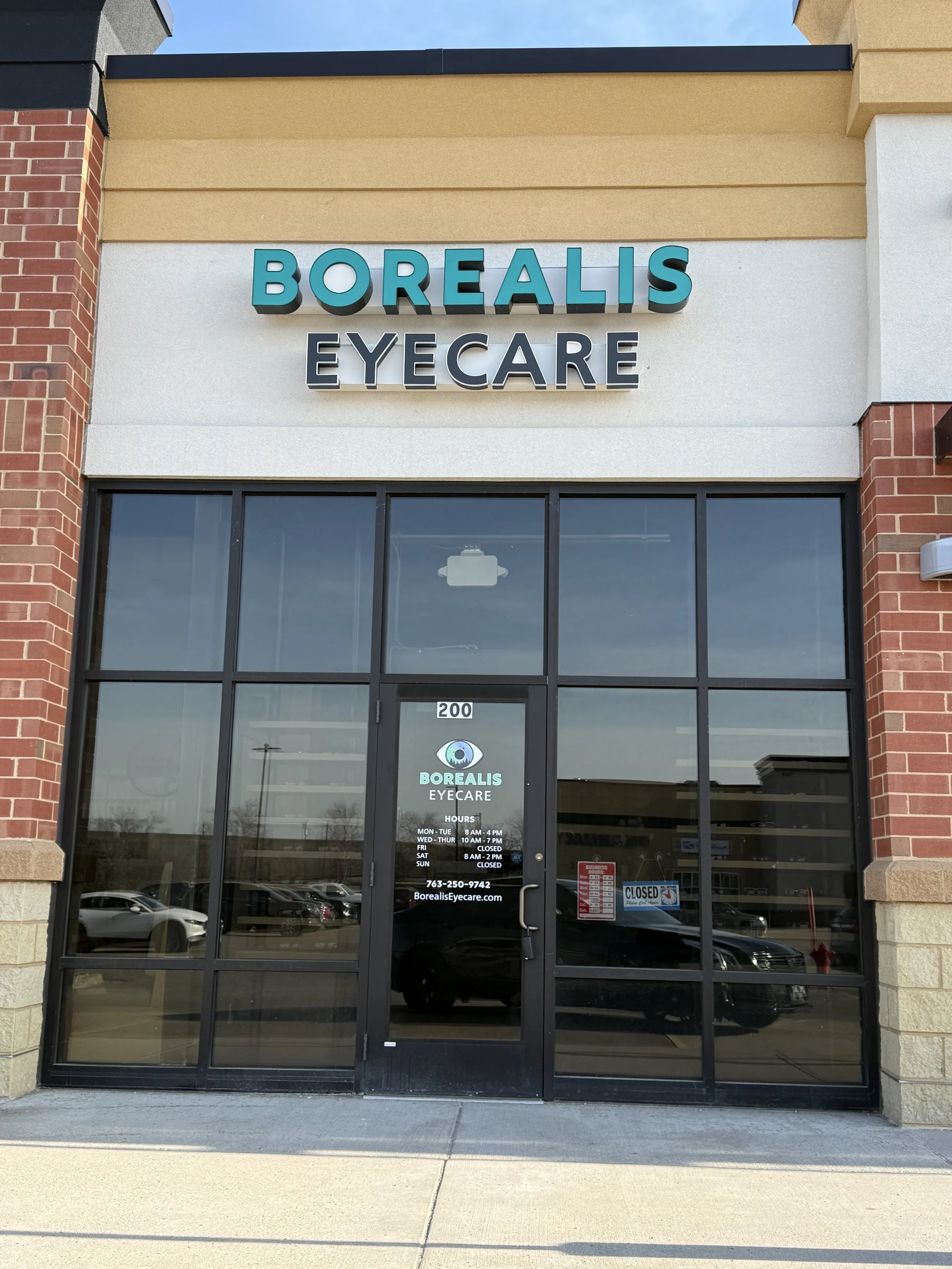 Storefront of Borealis Eyecare with glass doors, signage indicating hours and contact info, and a 'Closed' sign.