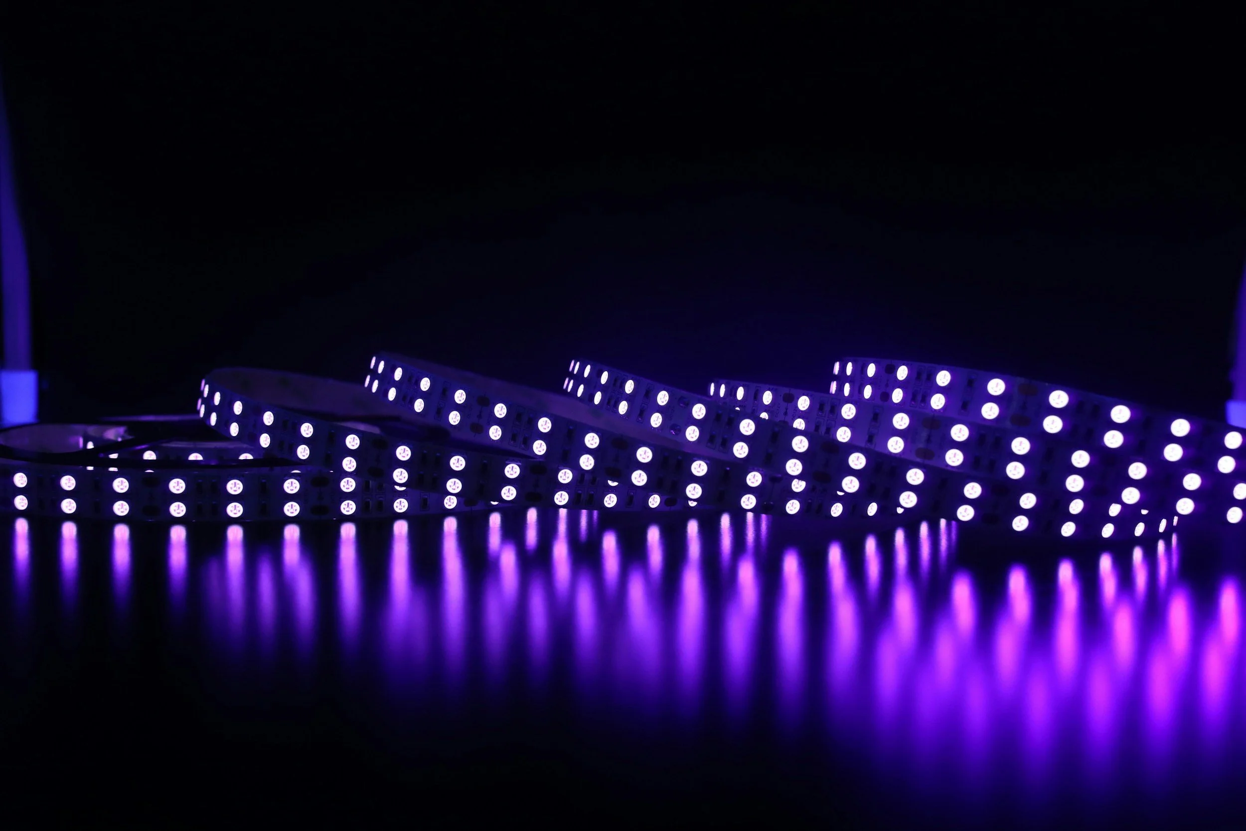 Purple LED strip lights on a reflective surface in a dark environment.