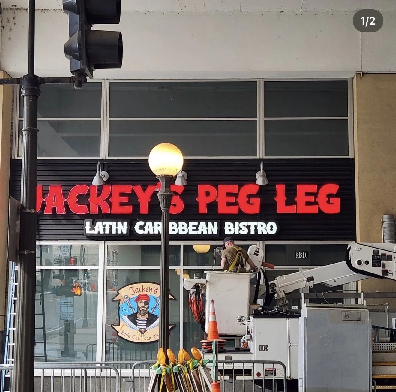 Sign for Jackey's Peg Leg Latin Caribbean Bistro with construction worker in front, street pole, and outdoor equipment.