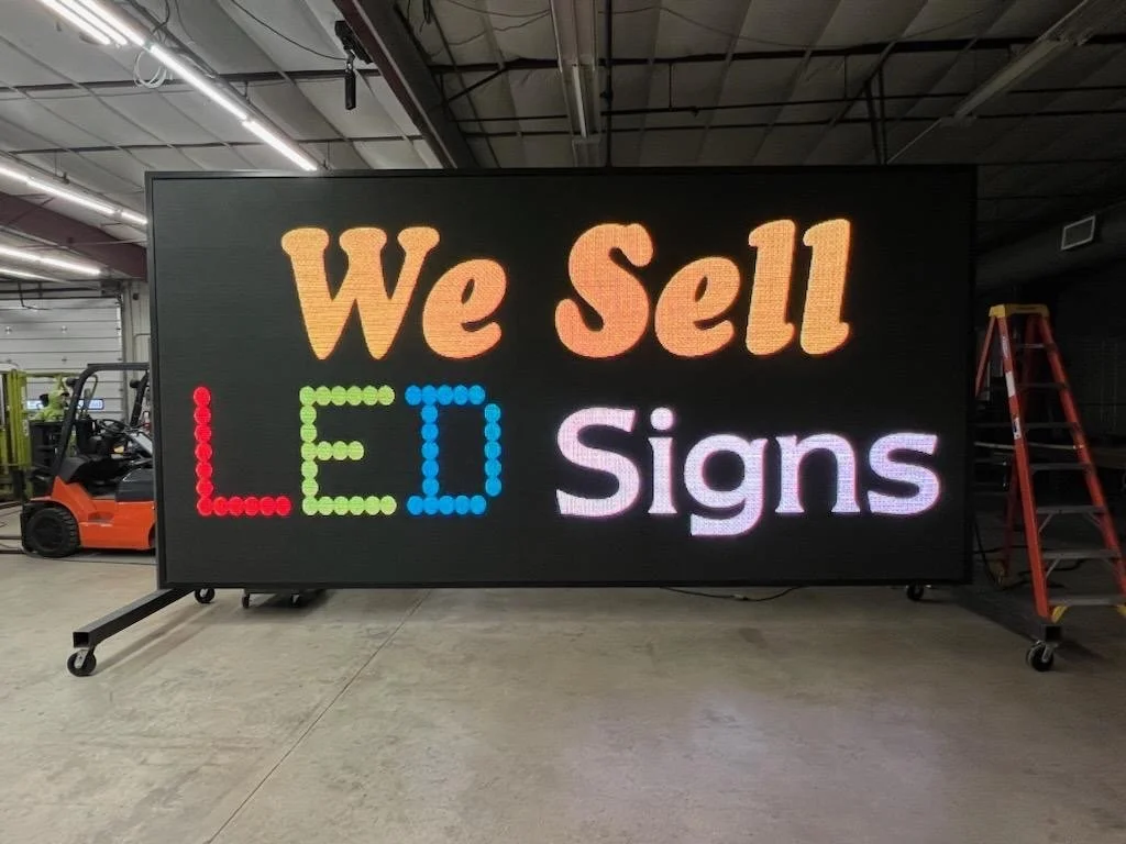 Large LED sign that says 'We Sell LED Signs' in colorful letters, located in a warehouse or workshop setting.