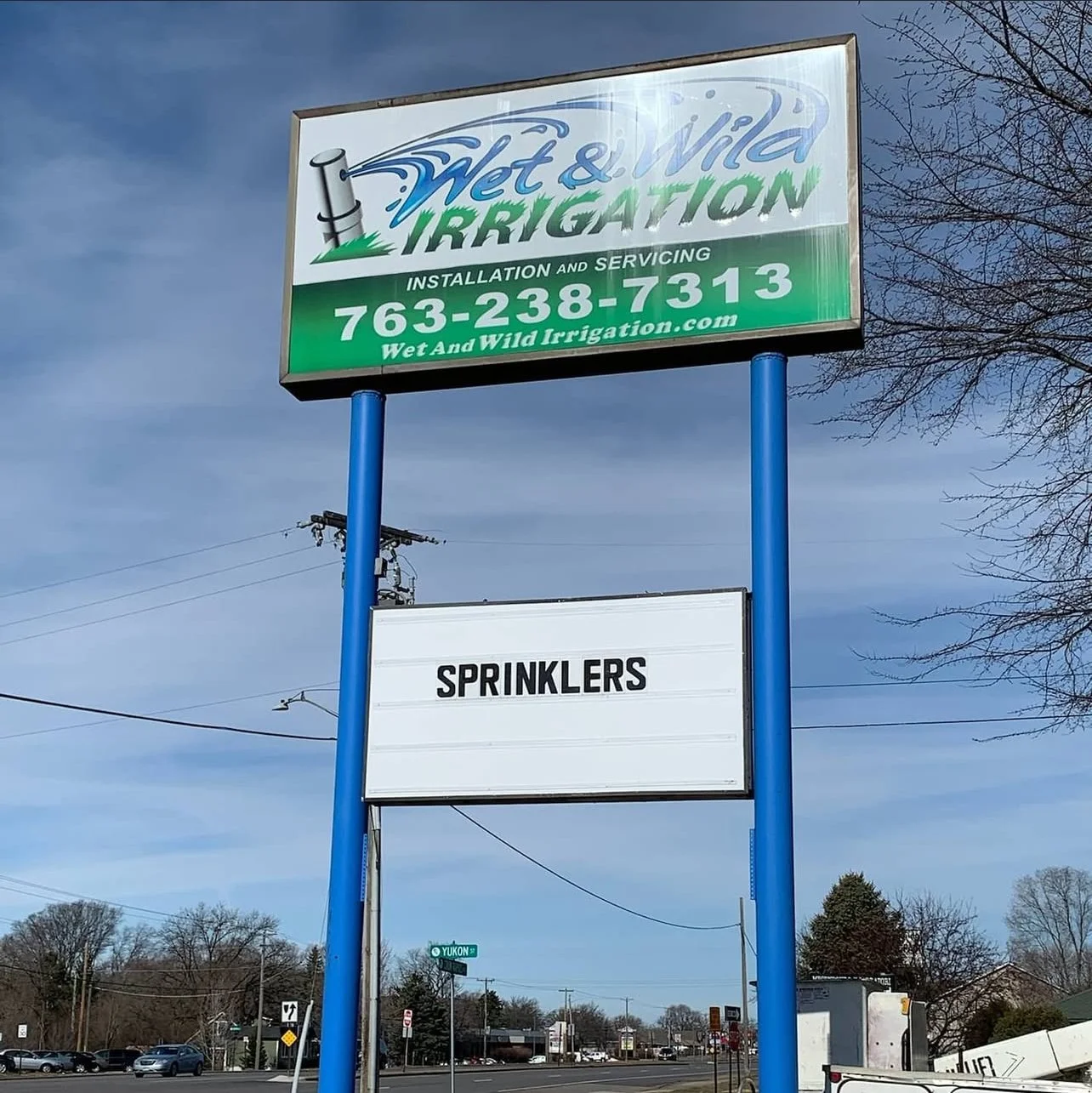 Outdoor sign for Wet & Wild Irrigation with contact information, and a blank sign below labeled 'Sprinklers'.