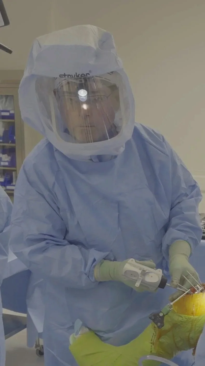 Dr. Randall Schultz, a board-certified orthopedic surgeon with 30 years of experience, performing a joint replacement procedure in full protective gear.