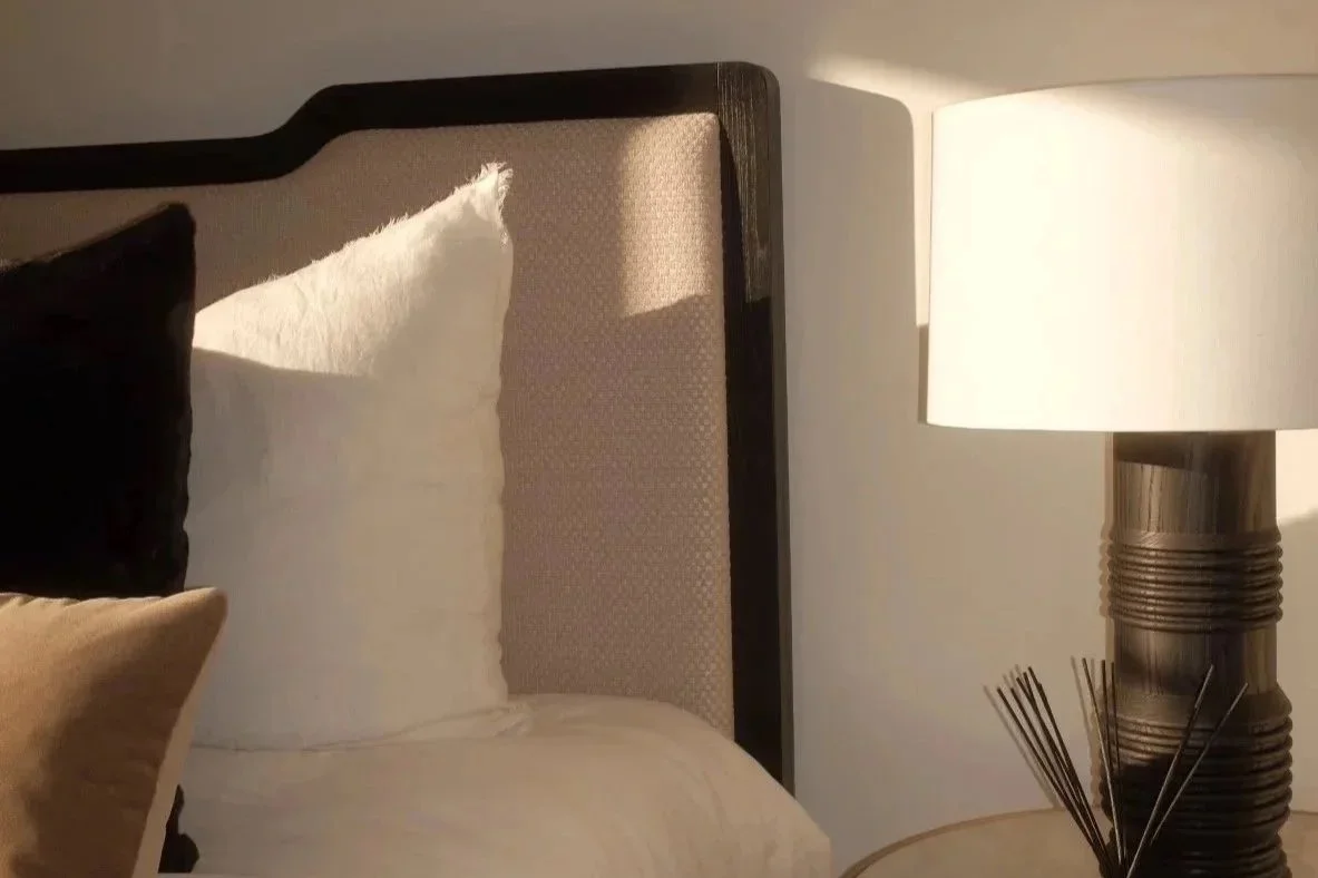 Close-up of a bed with white pillows and a black pillow, next to a nightstand with a modern lamp.