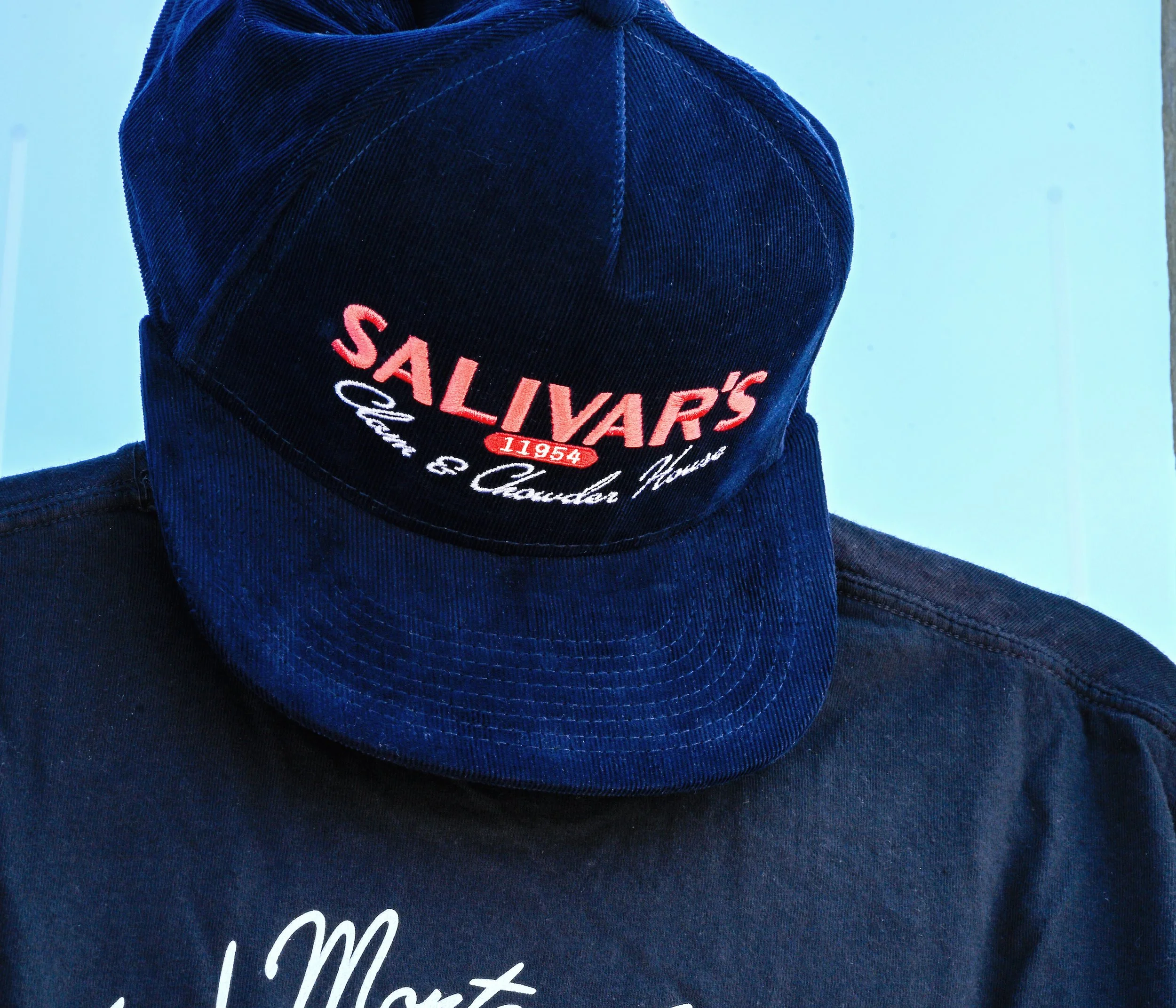 Close-up of a dark blue baseball corduroy hat with embroidered 'Salivar's' logo.