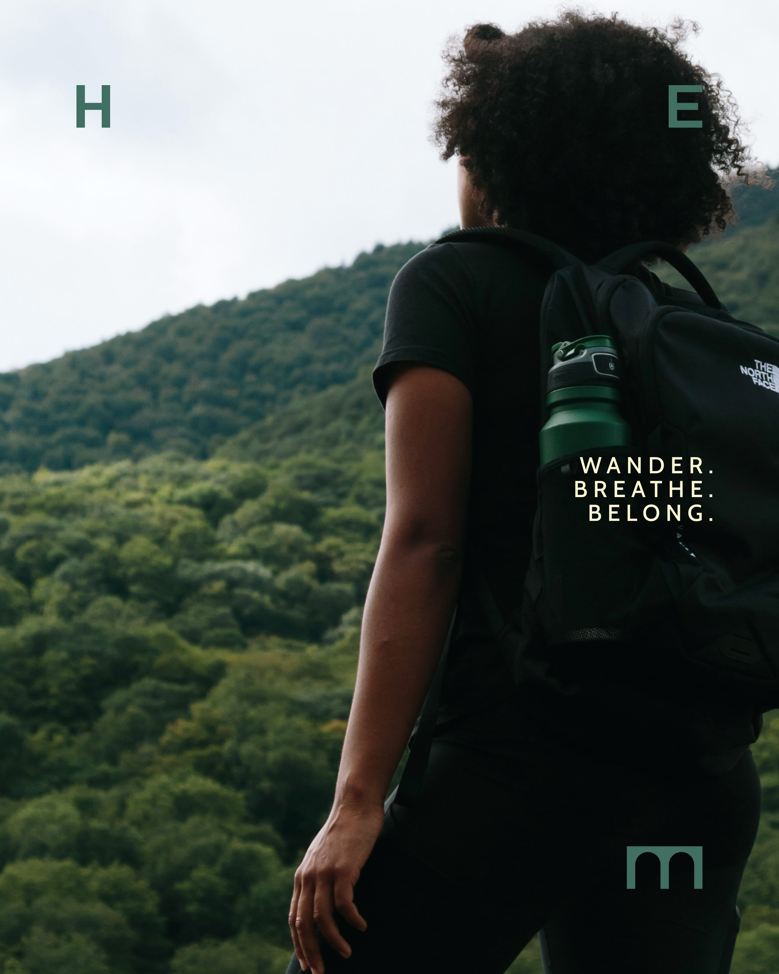 A woman with curly hair wearing a black shirt and hiking backpack standing outdoors near green hills, with the text "WANDER. BREATHE. BELONG." and "HEM" logo overlaid on the image.