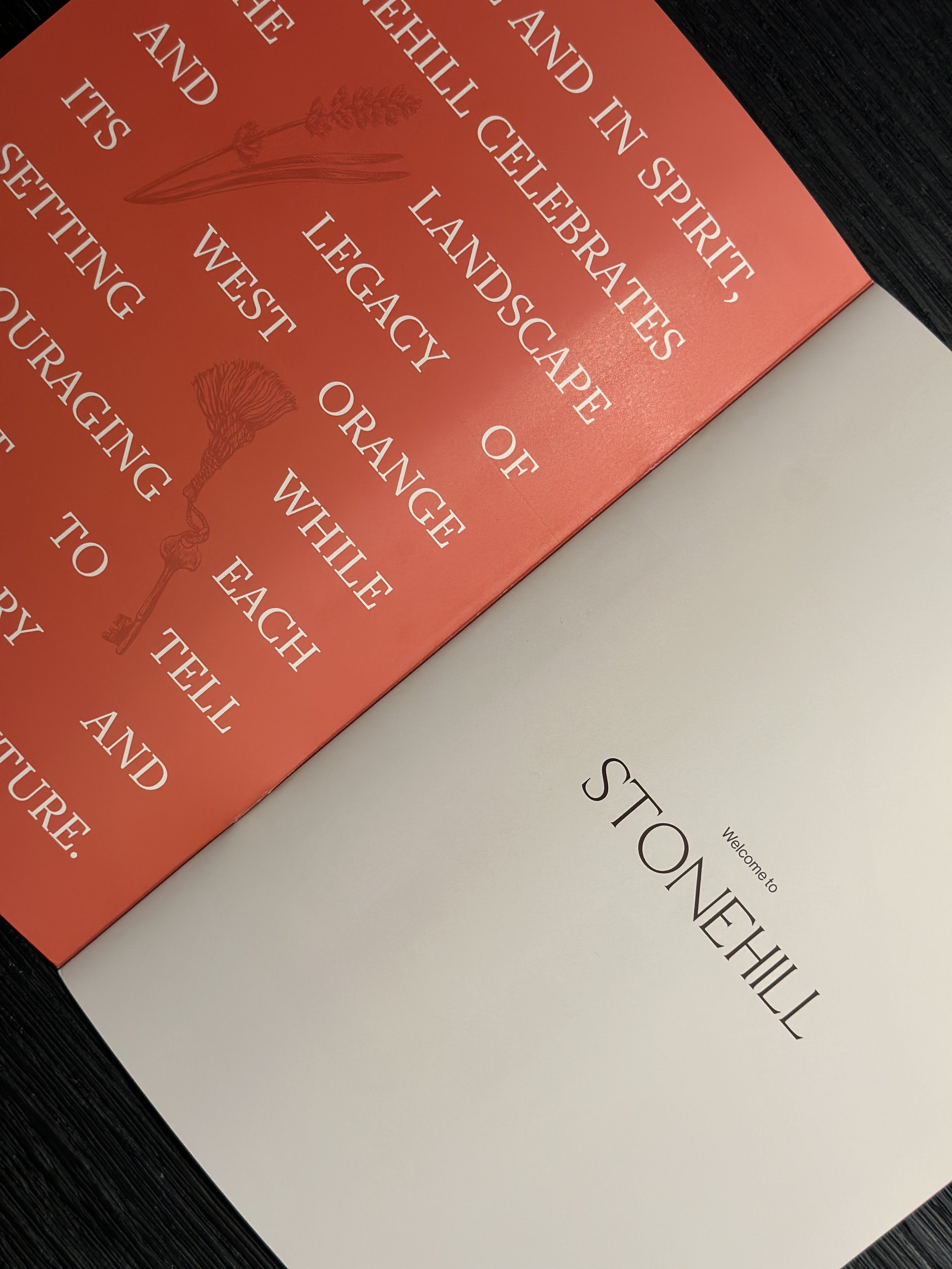 A close-up of a brochure for Stonehill apartments, containing a poem in white ink text and illustrations of lavender, and a white page visible that reads 'Welcome to Stonehill'.