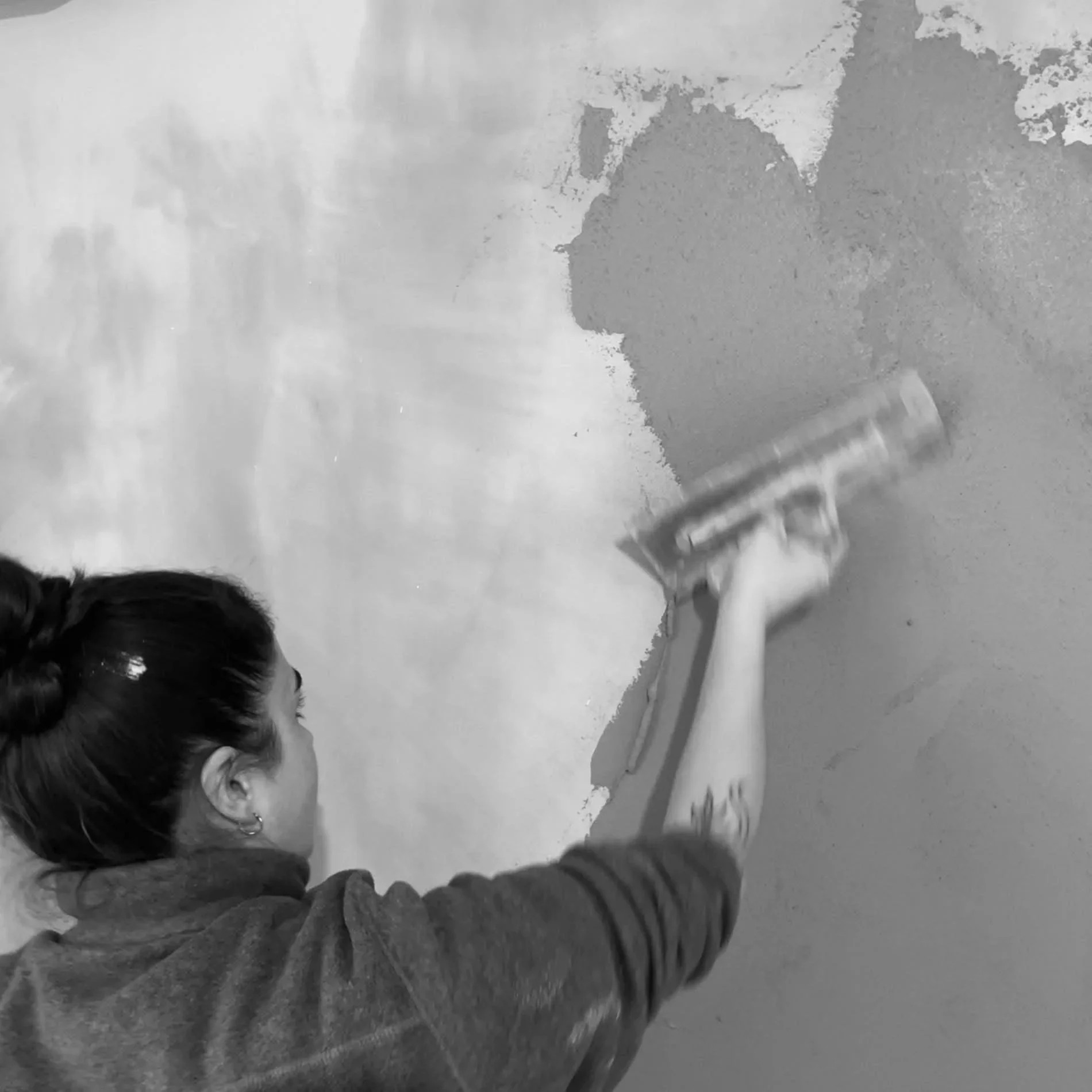 Une femme en train de peindre un mur avec une brosse à peinture, en noir et blanc.