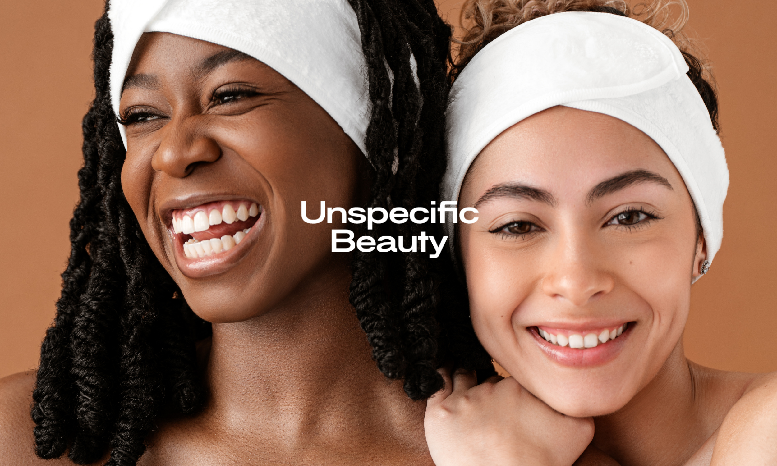Close-up portrait of two smiling women with headbands, one with dark curly hair and the other with light brown hair, against a brown background. Text overlay says 'Unspecific Beauty'.